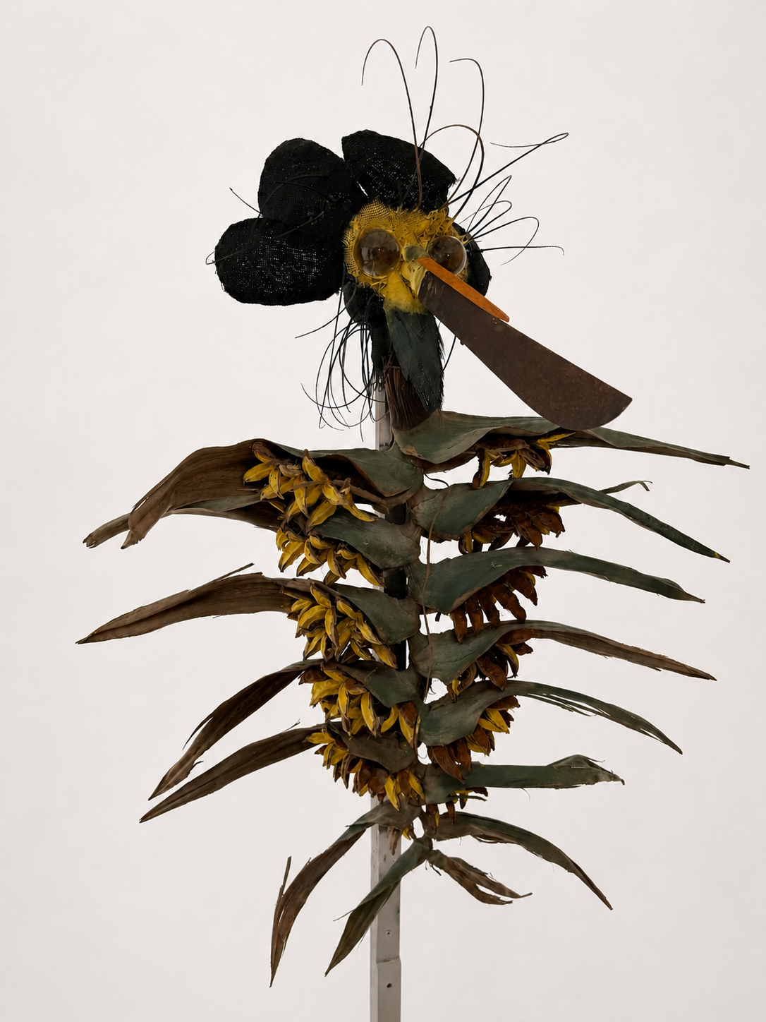 Clea / 2019-2026 / Materials: Machete, two spherical crystal decanter tops, royal poinciana stems, wire, painted burlap, paint, Traveler's Palm tree material, wood pillar repurposed from decorative wedding arch