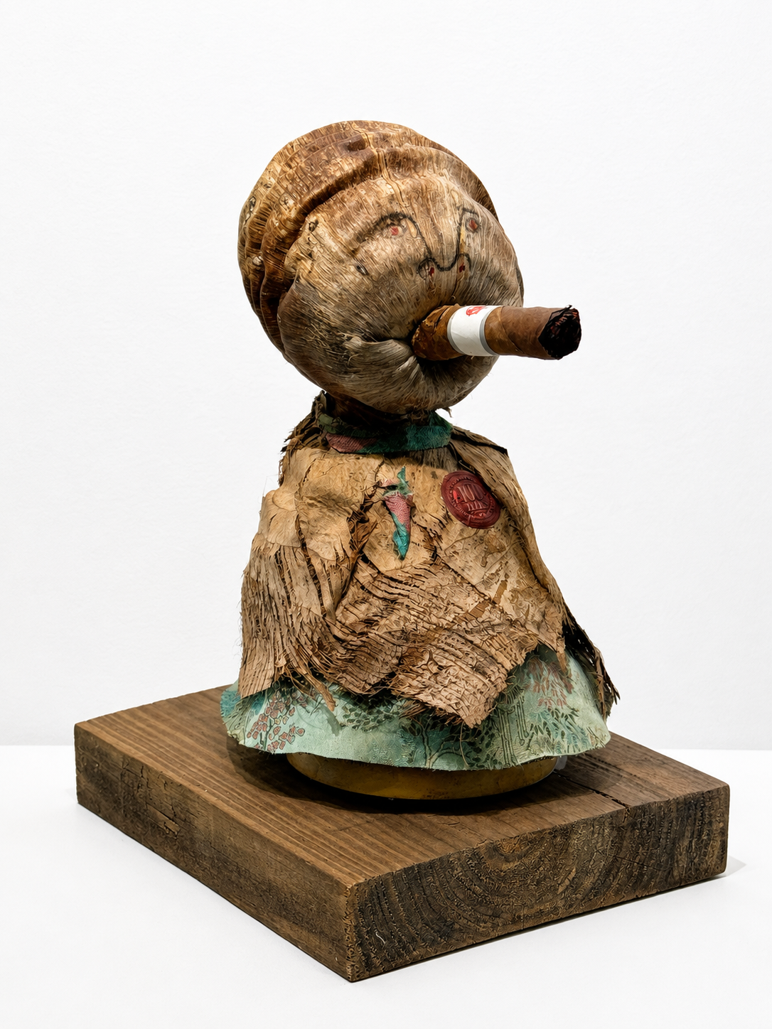 Doña Carmela / 2024 / Materials: Coconut, microphone stand, marker, coconut tree material, repurposed fabric from the cover of a diary, cigar, pielroja wrapper, wood base