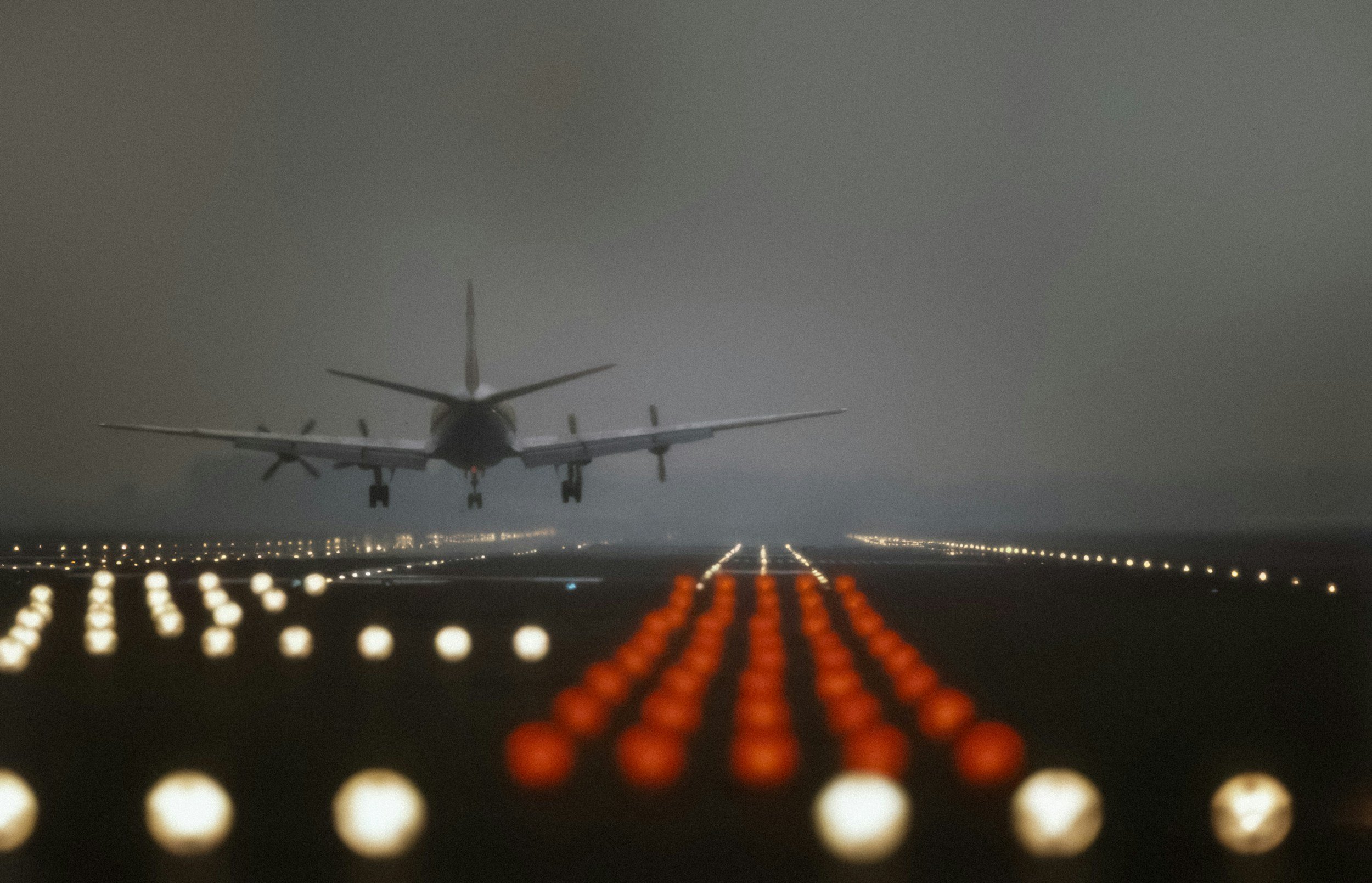 An airplane approaching a runway at night, seen from the perspective of the cockpit or front of the aircraft with illuminated runway lights visible.