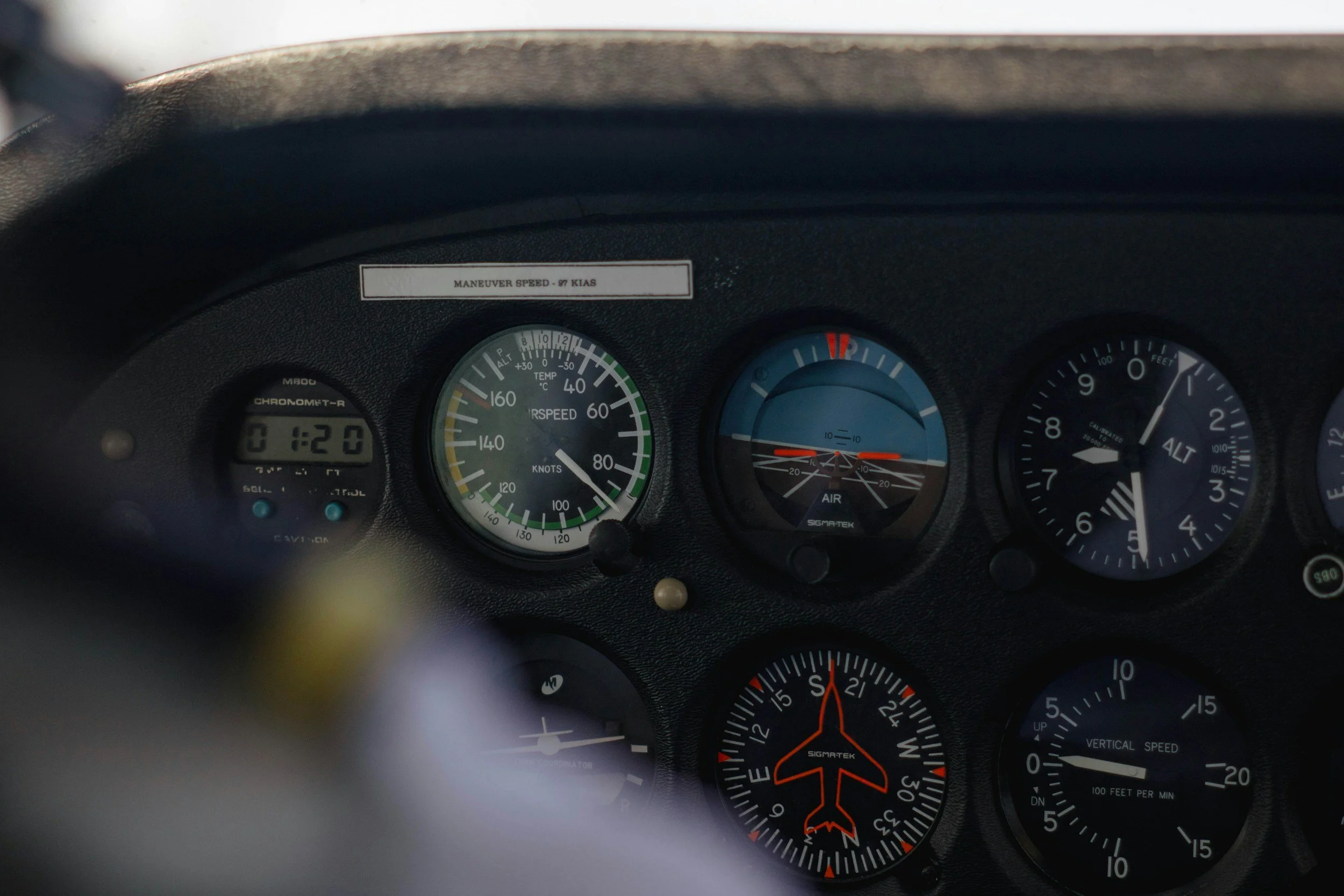 Car dashboard showing gauges for speed, temperature, and altitude, with a sticker displaying 'MANEUVER SPEED - 97 KIAS' and an orange airplane indicator.