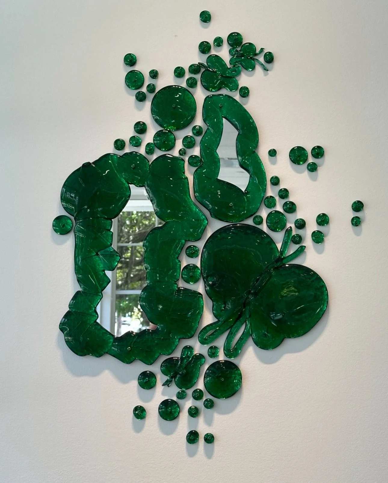 Decorative wall art made of green glass pieces arranged in the shape of a beetle with a large round body, a smaller round head, and long antennae, surrounded by smaller glass dots.