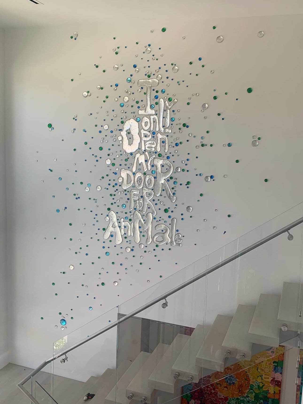 Decorative wall installation with shiny, metallic letters spelling out 'I only run for animal' and surrounded by scattered blue, green, and silver reflective circles, located above a staircase in a modern interior.