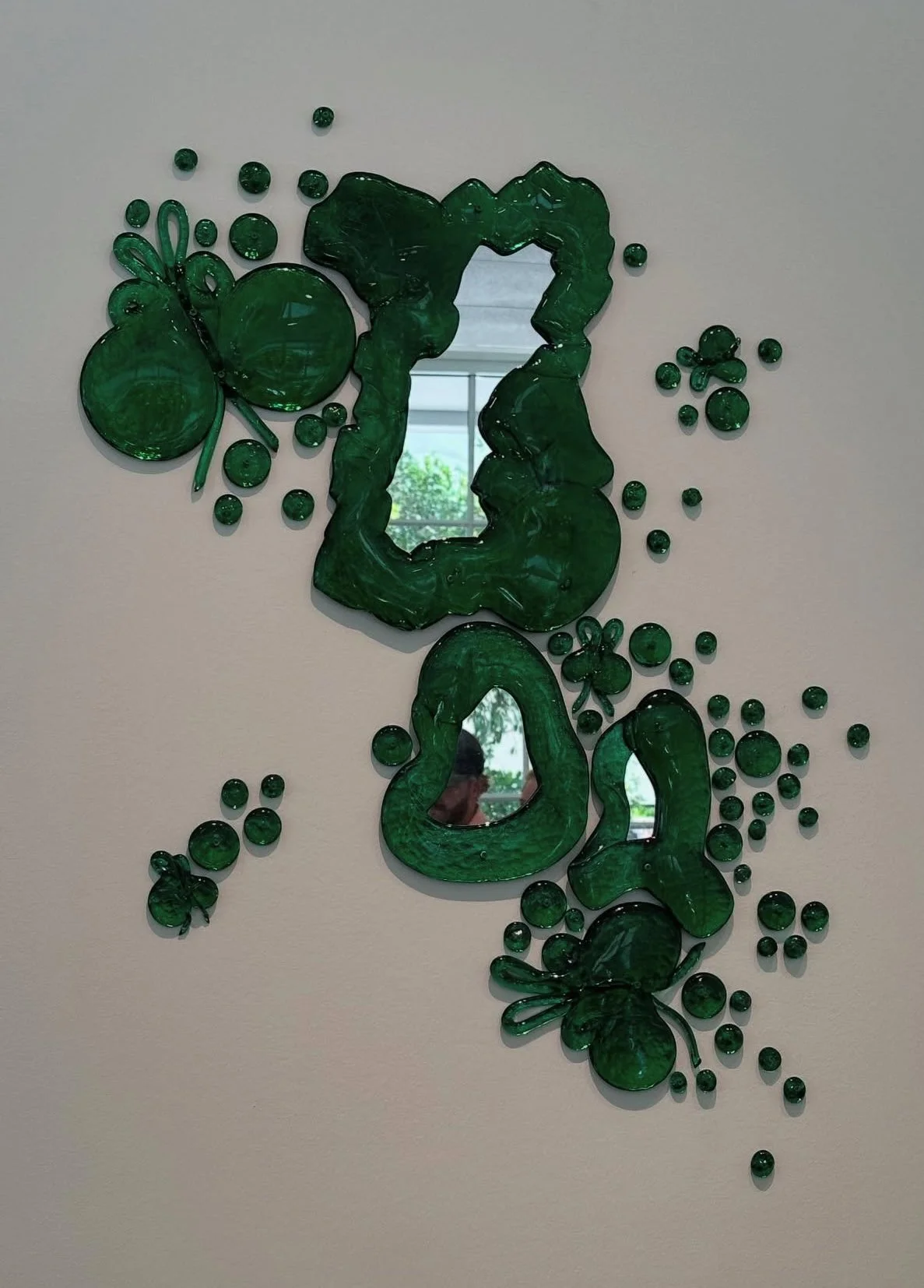 Decorative mirror with green glass ocean-themed embellishments, including starfish, seashells, and bubbles, mounted on a white wall.