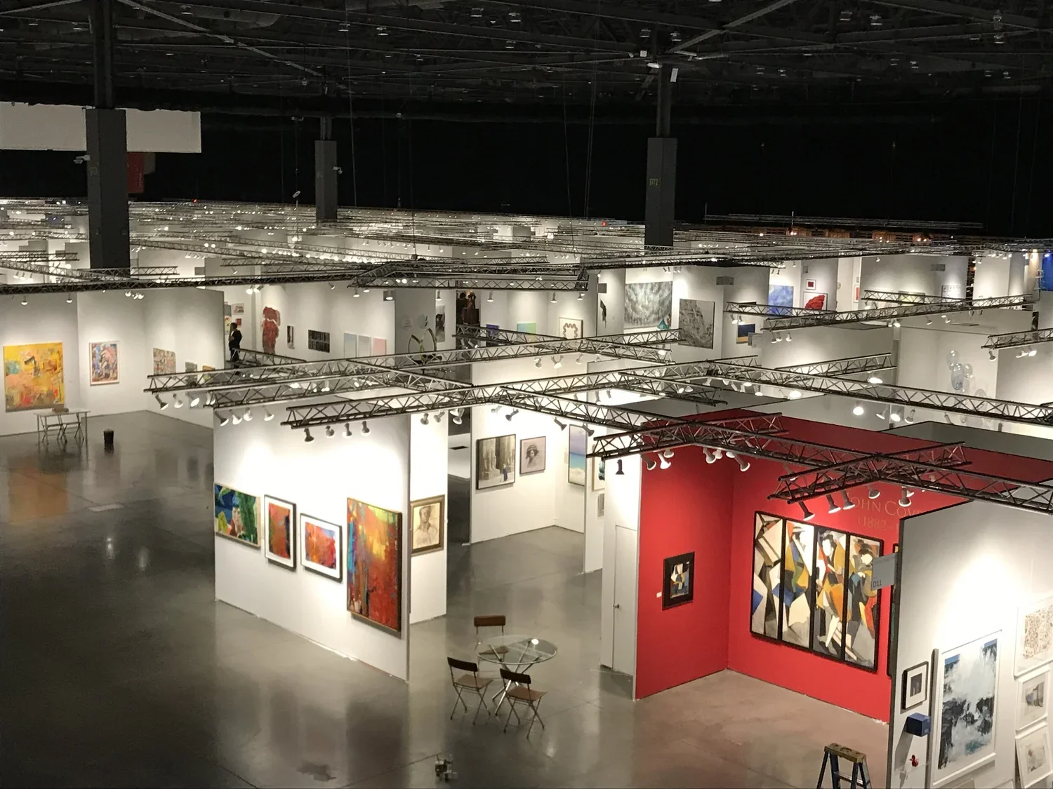 An art gallery with white walls displaying various paintings, some abstract and others realistic, lit by track lighting on the ceiling.