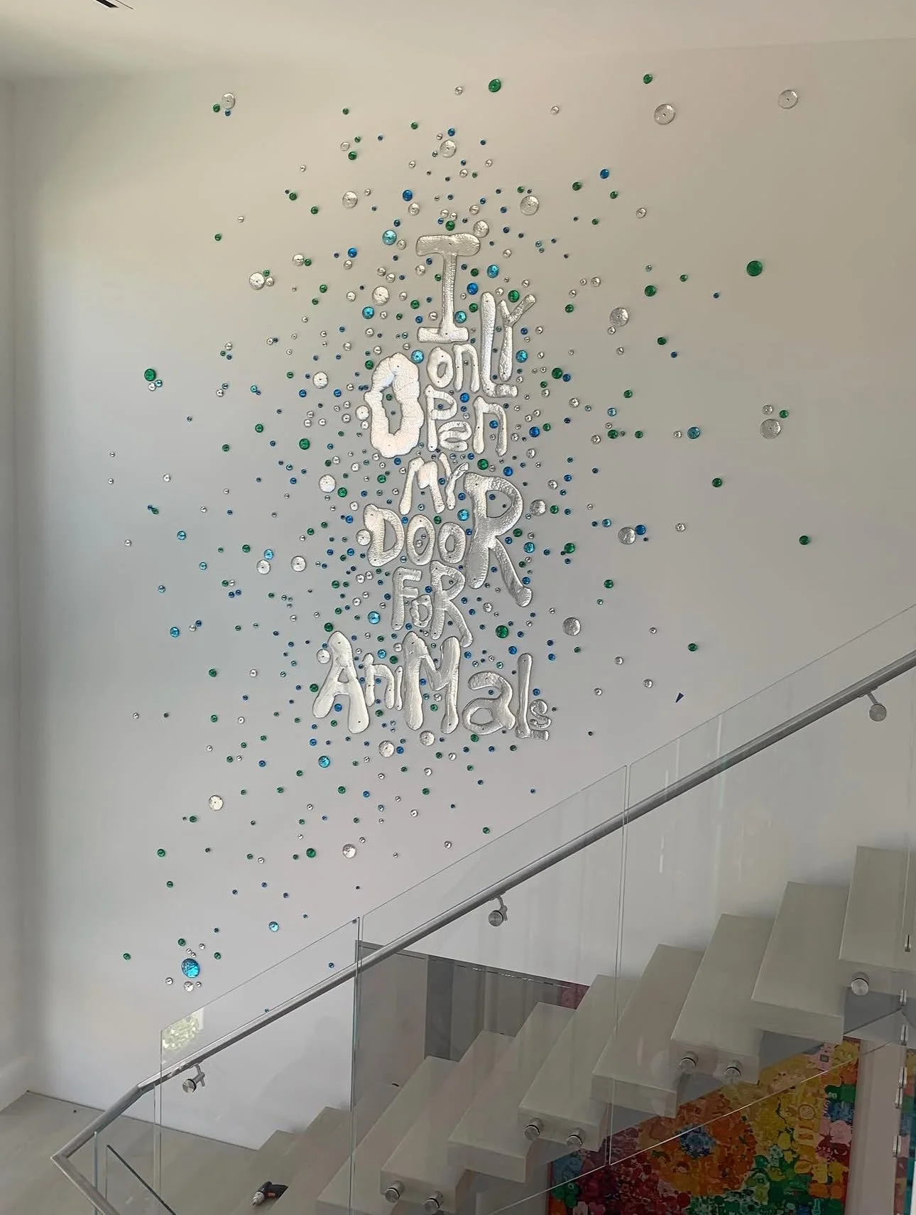 Decorative wall with silver, green, blue, and clear balloons surrounding silver lettering that reads 'I only open for animals' in a modern interior space with stairs and colorful wall art.
