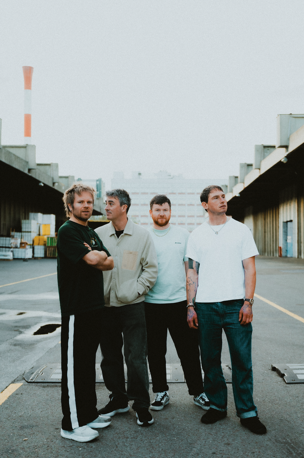 Enter Shikari Band standing in an industrial area with warehouses and a smokestack in the background.