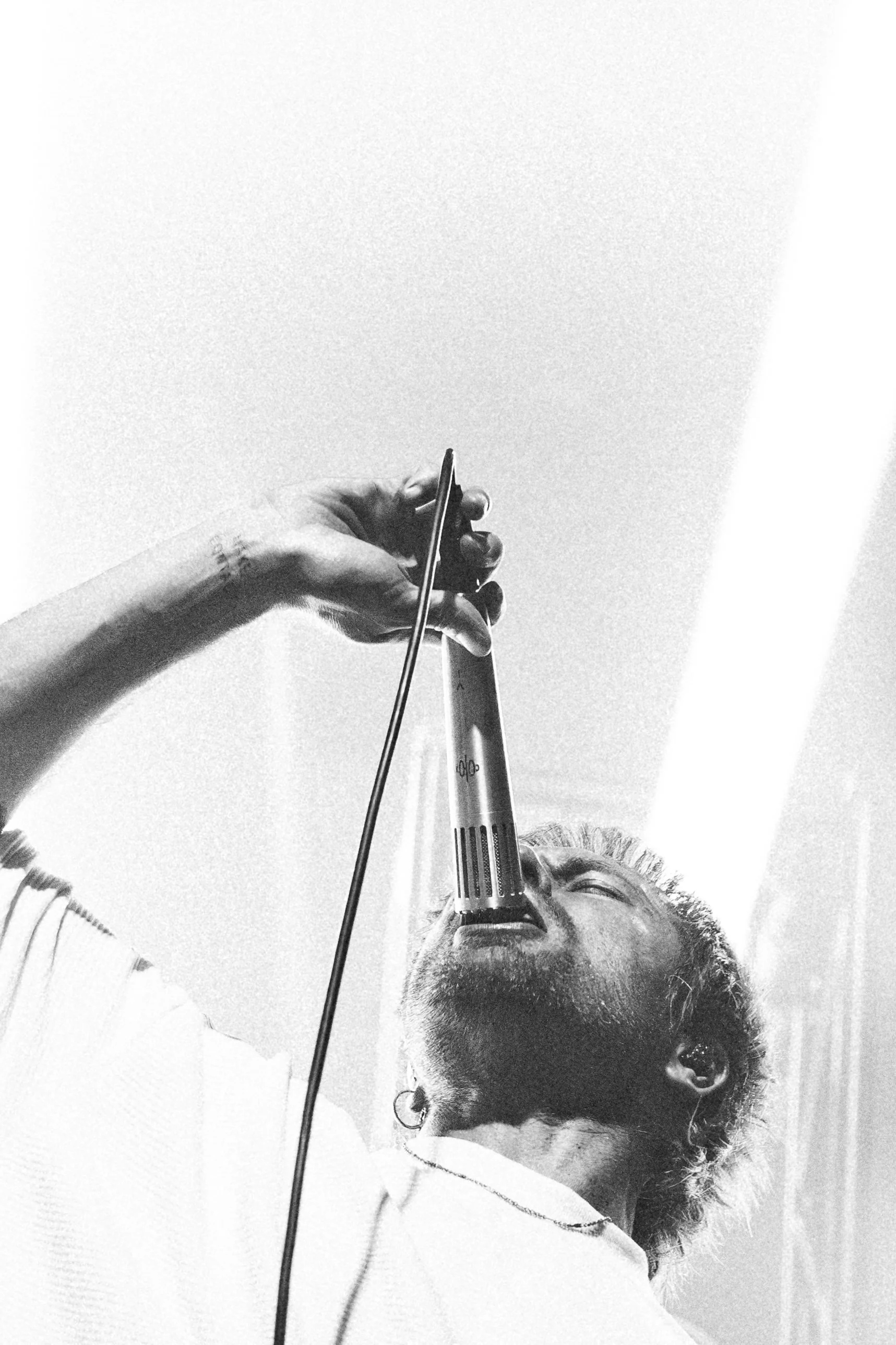 Black and white photo Rou from enter shikari with glasses and earrings singing into a microphone from a low angle.