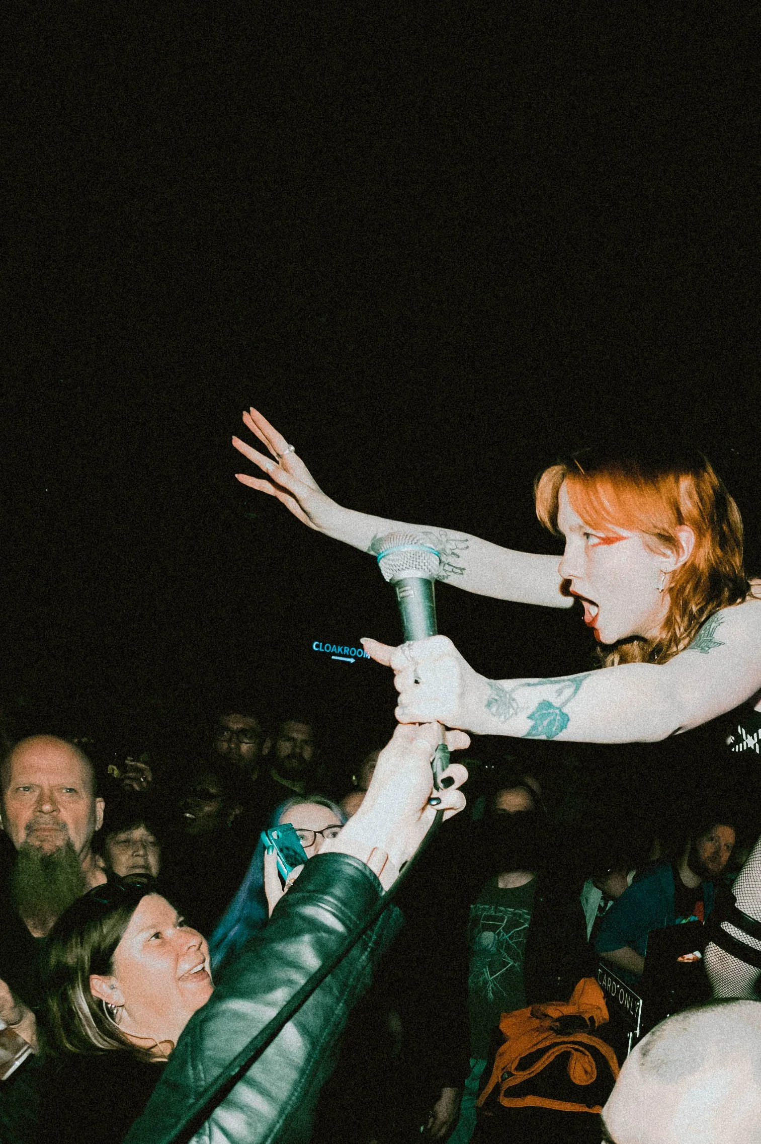 Witch Fever Singer A woman with tattoos on her arm and long red hair is reaching out to a crowd that is gathered around her. She appears to be performing or speaking into a microphone.