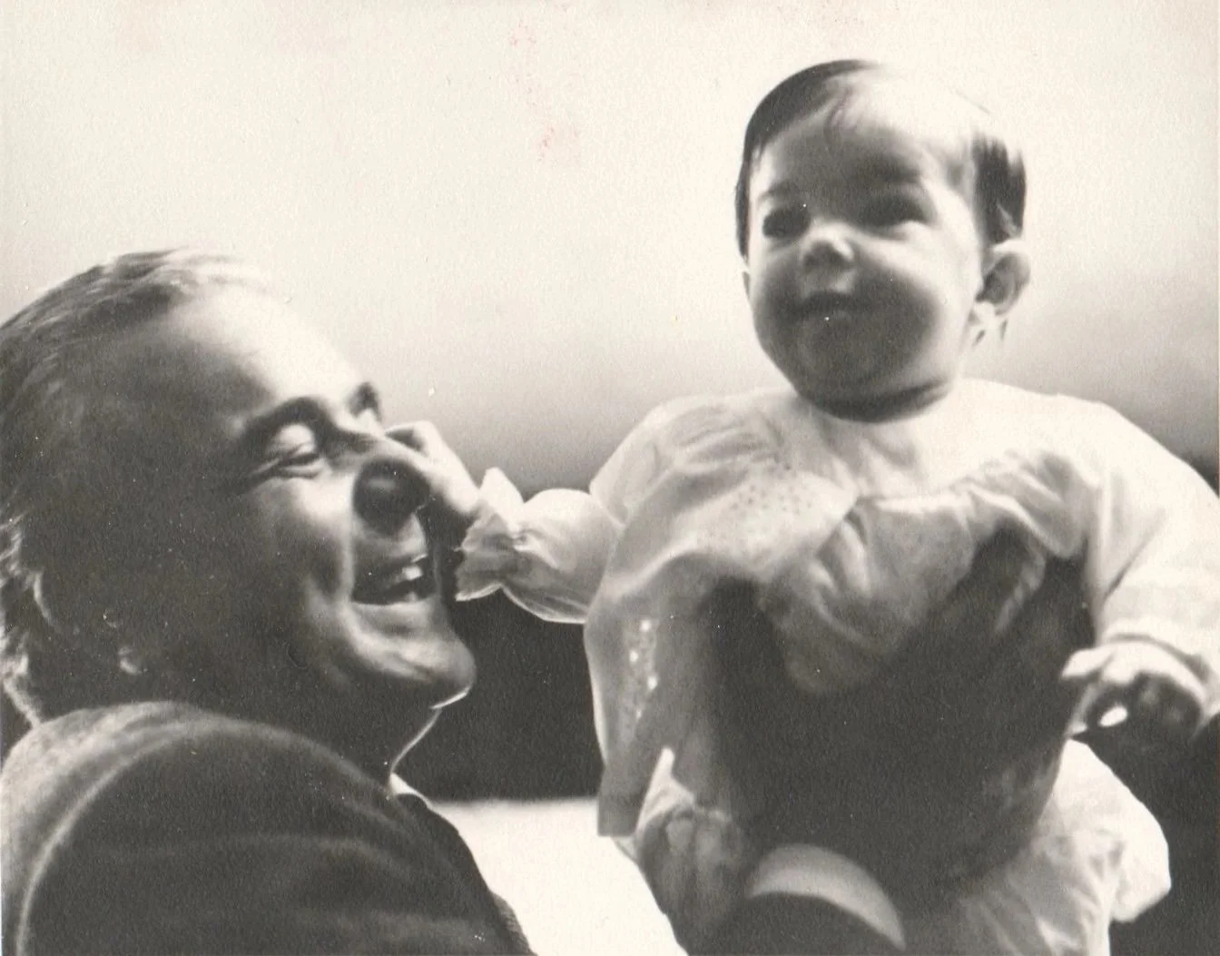 John smiling and holding baby Linda, who is reaching towards her face, in a black-and-white photo.