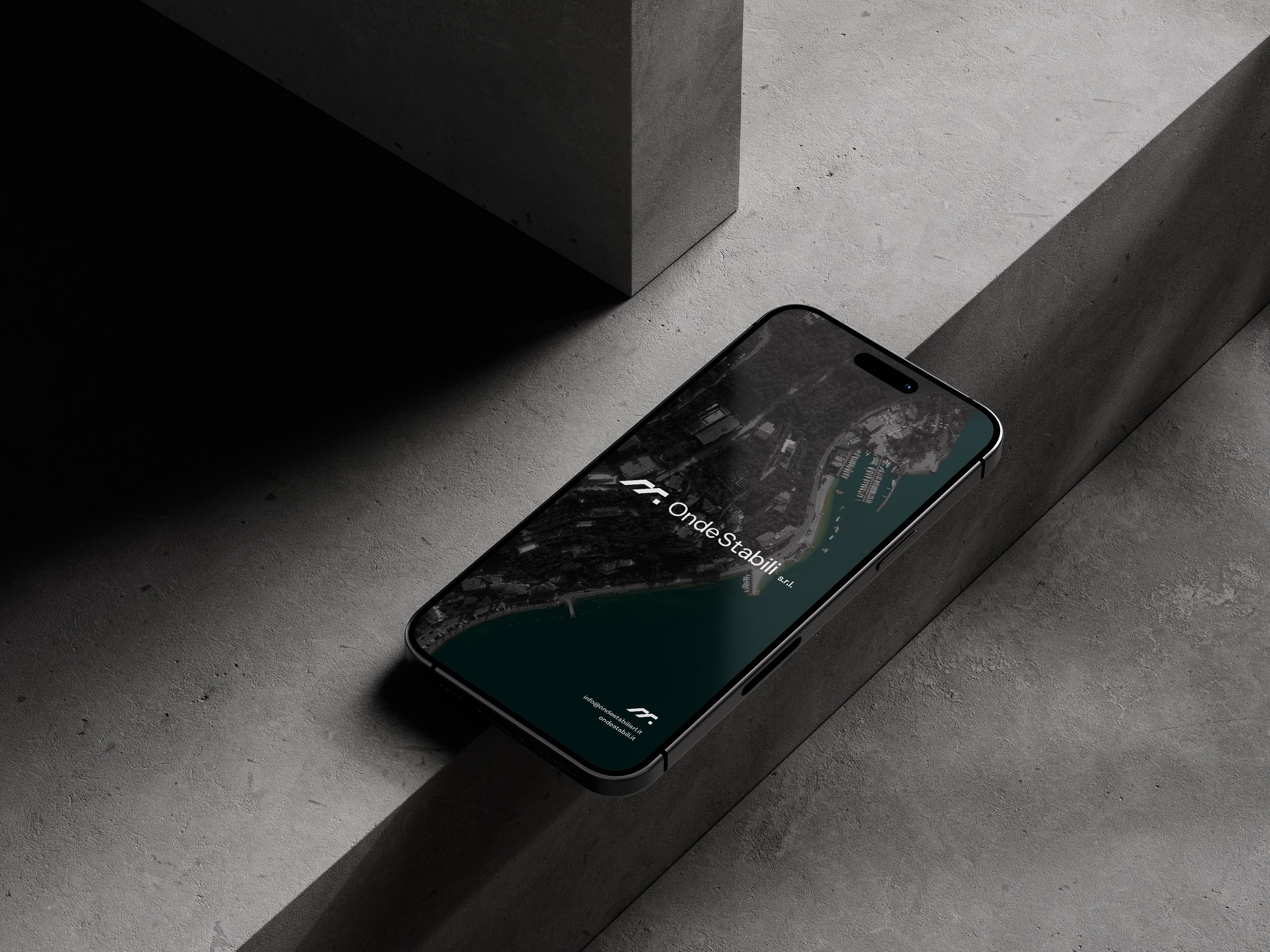 A smartphone lying on a dark, textured surface, displaying a map or navigation app with the text "OndeStabillit".