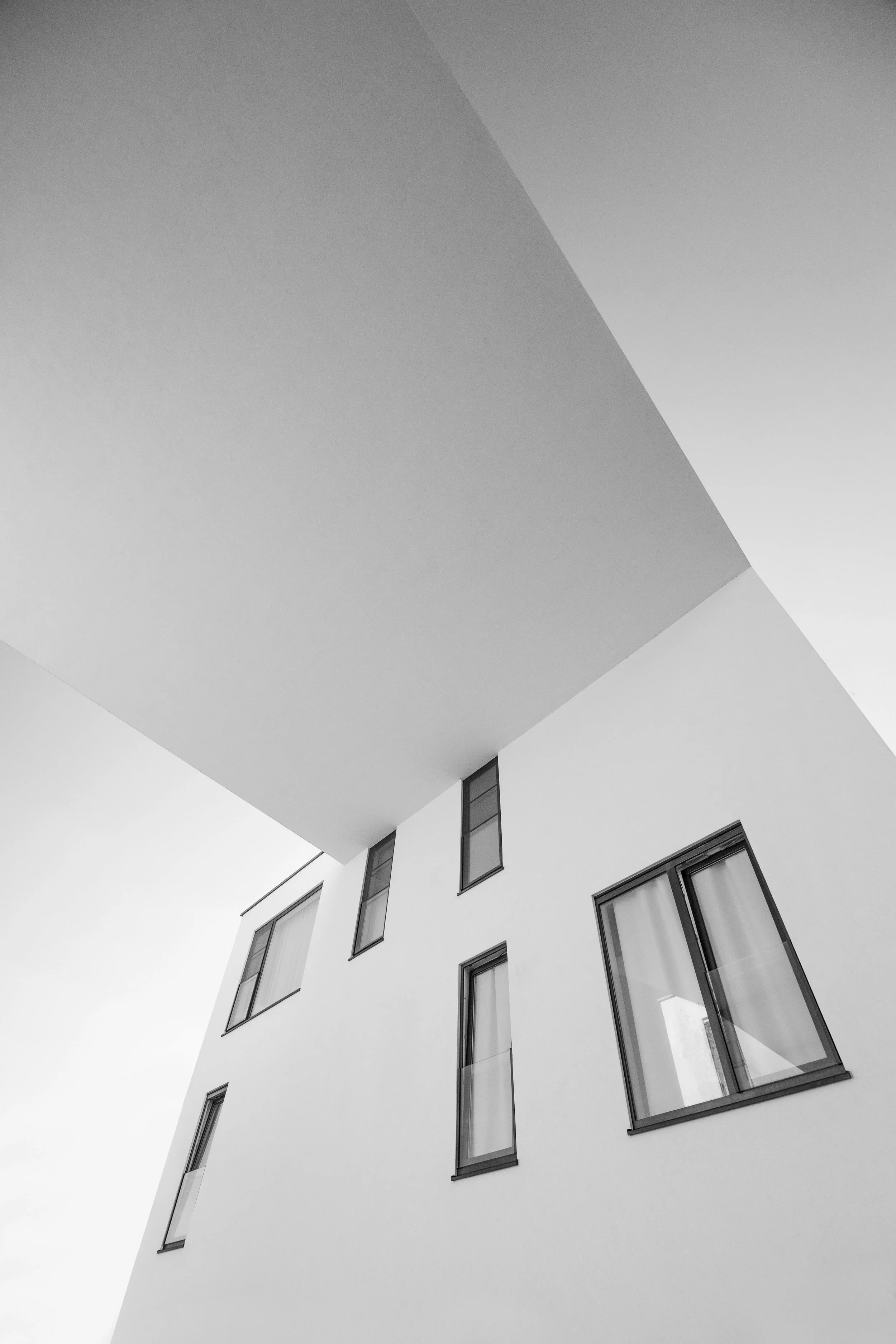The photo features a modern building with white walls and multiple windows, taken from a low angle looking upward, emphasizing the building's clean lines and geometric shapes.
