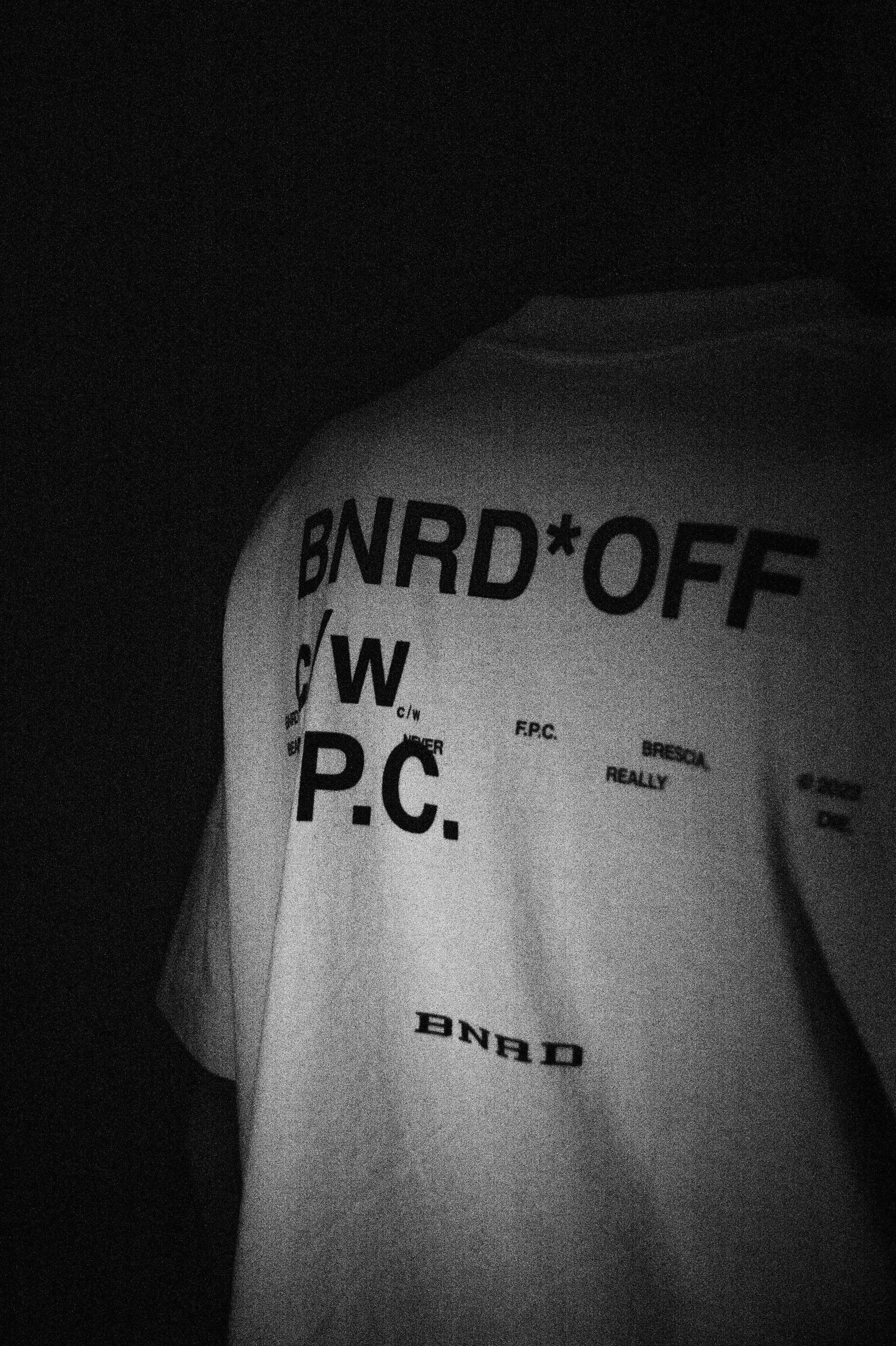 Close-up of a person wearing a T-shirt with partially visible text, in black and white, with dark background.