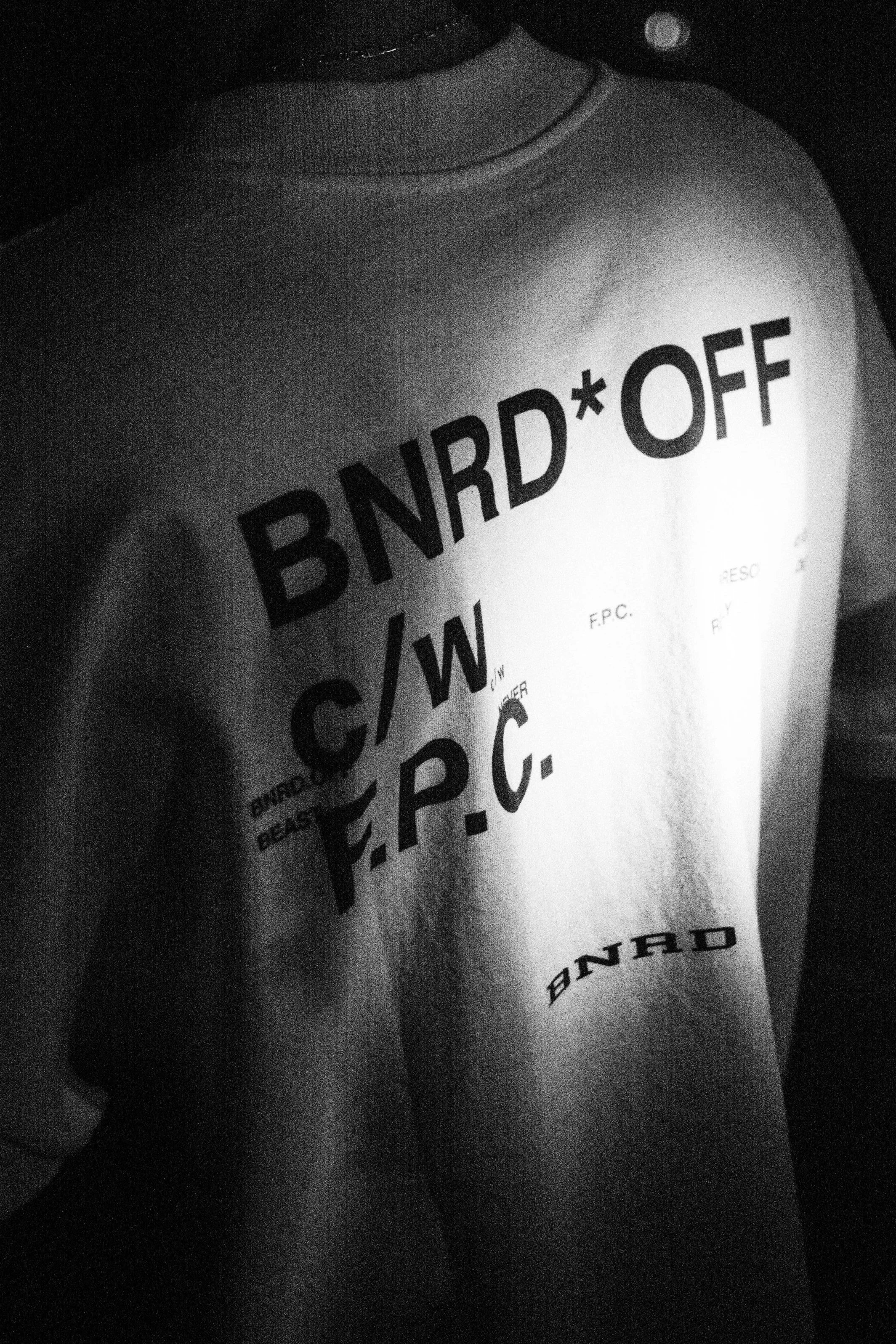 Close-up of a person wearing a T-shirt with the words 'BRAND*OFF' printed on it, in black and white.