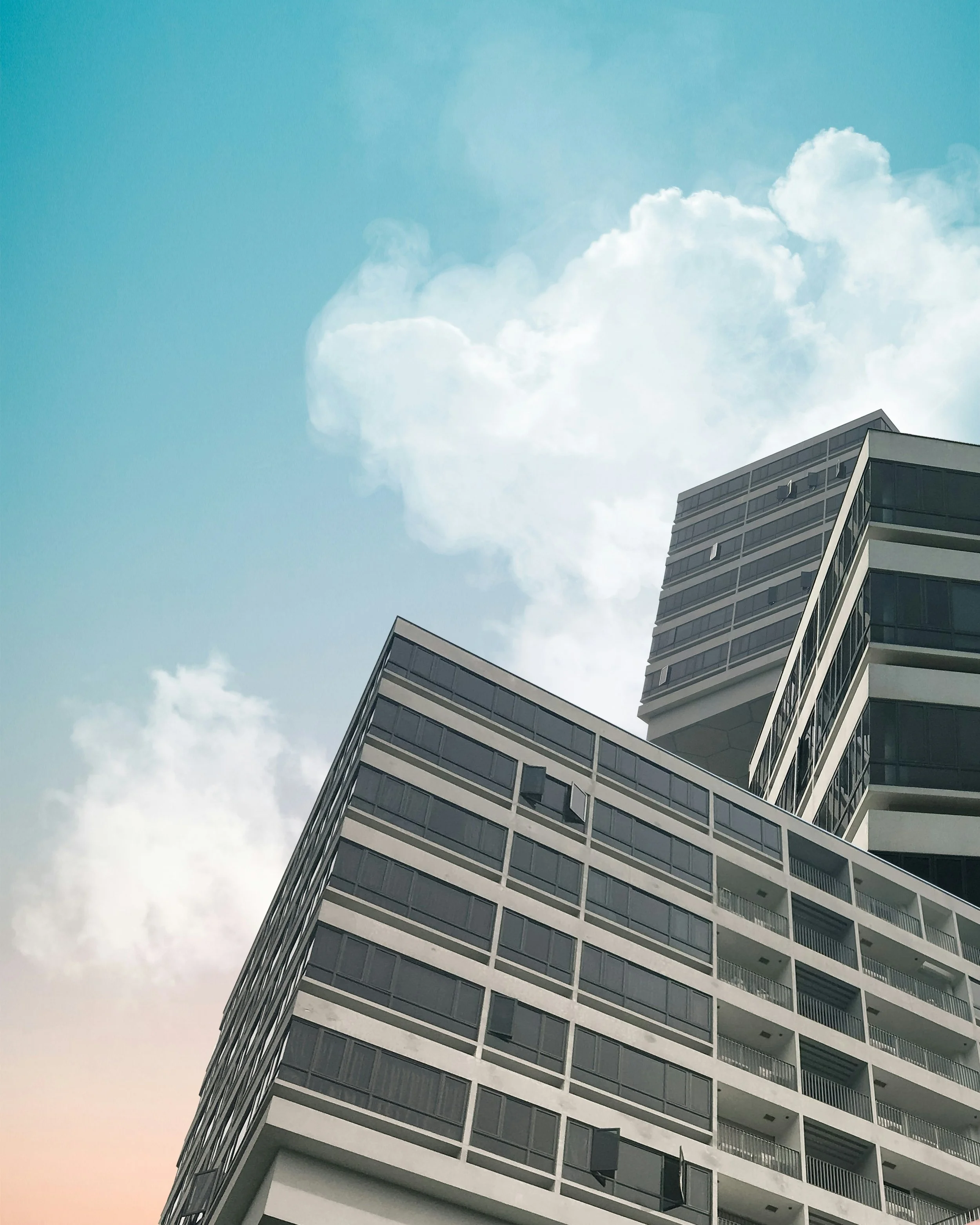 Modern multi-story apartment building with glass balconies against a partly cloudy sky.