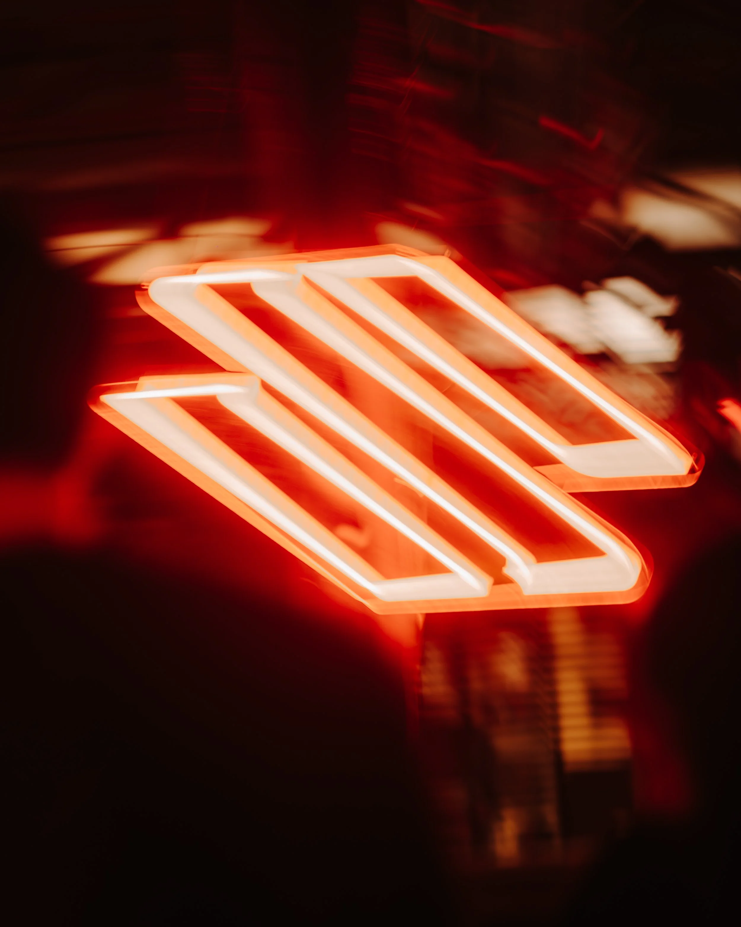 Close-up of a neon sign with orange and white lights against a dark background, creating a blurred, glowing effect.