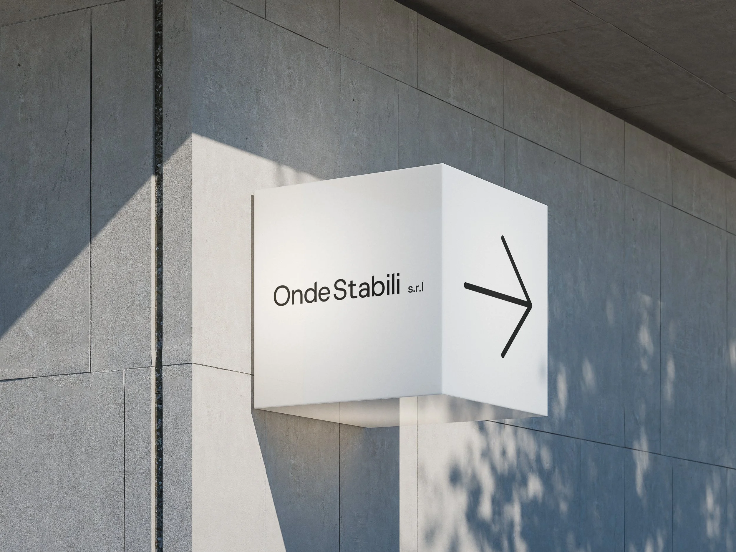 A modern white sign with black text on a light gray stone building wall. The sign has an arrow pointing to the right and shows the words 'Onde Stabili s.r.l.'.