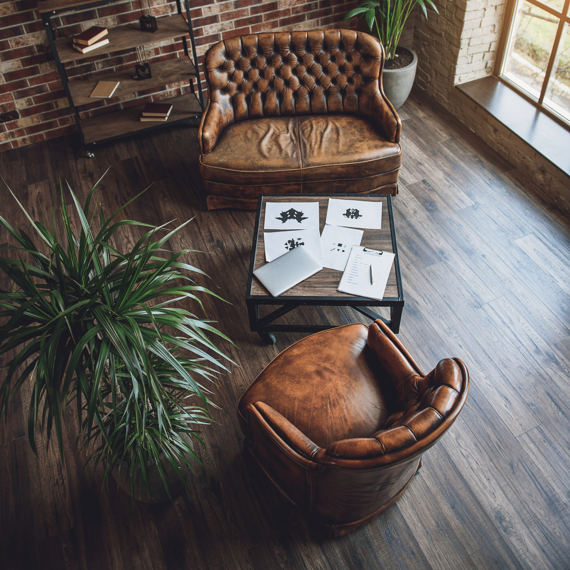 Leather armchair in a room with wooden floor, brick walls, shelves with books, and a large window with sunlight streaming in.