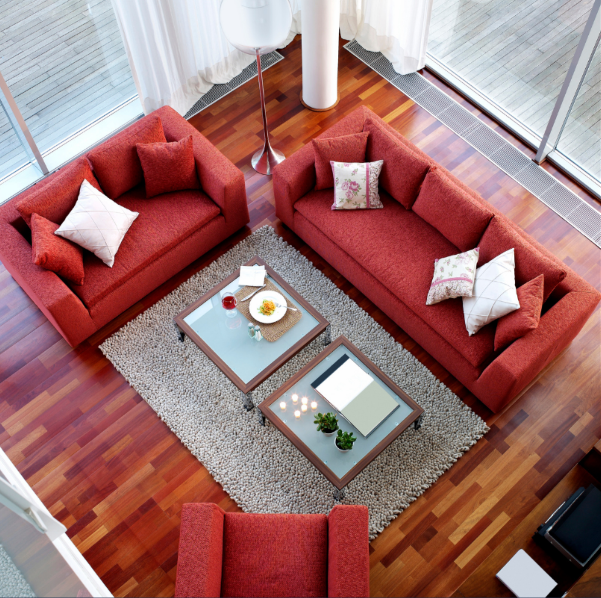 Living room with red sofas, a square glass-topped coffee table with snacks and drinks, and large windows with white curtains.