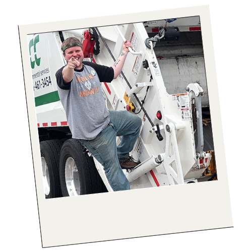 Person smiling and pointing at the camera while sitting on a trash truck.