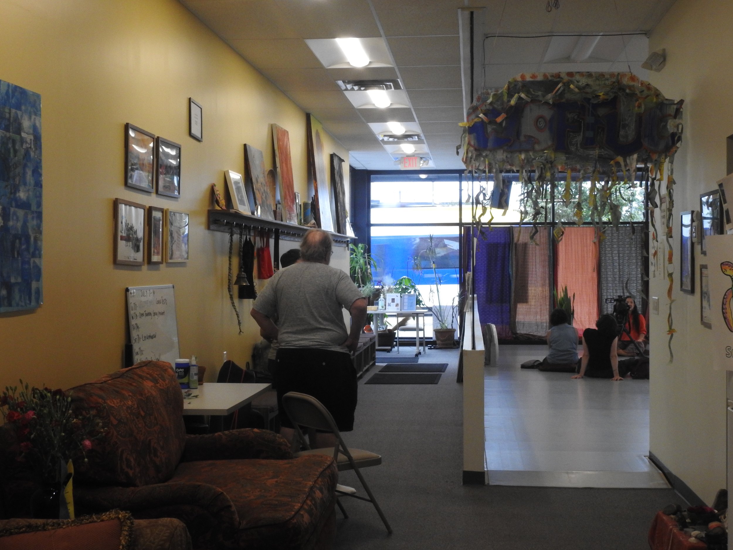 Interior photograph of Ananya Dance Theater. Some people stand to one side, while others sit on the floor next to the front window.