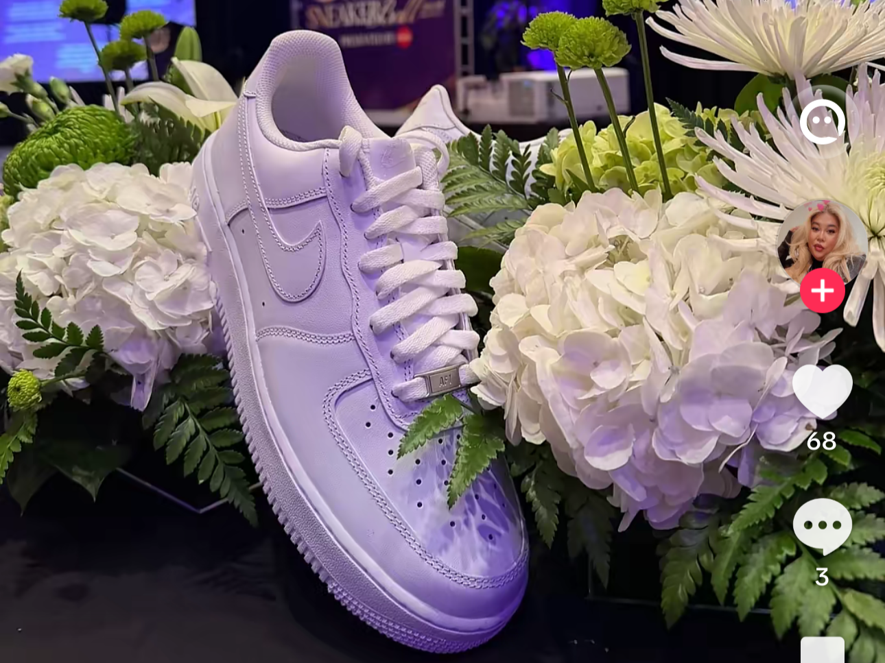 A white Nike sneaker placed among white and green flowers and leaves.