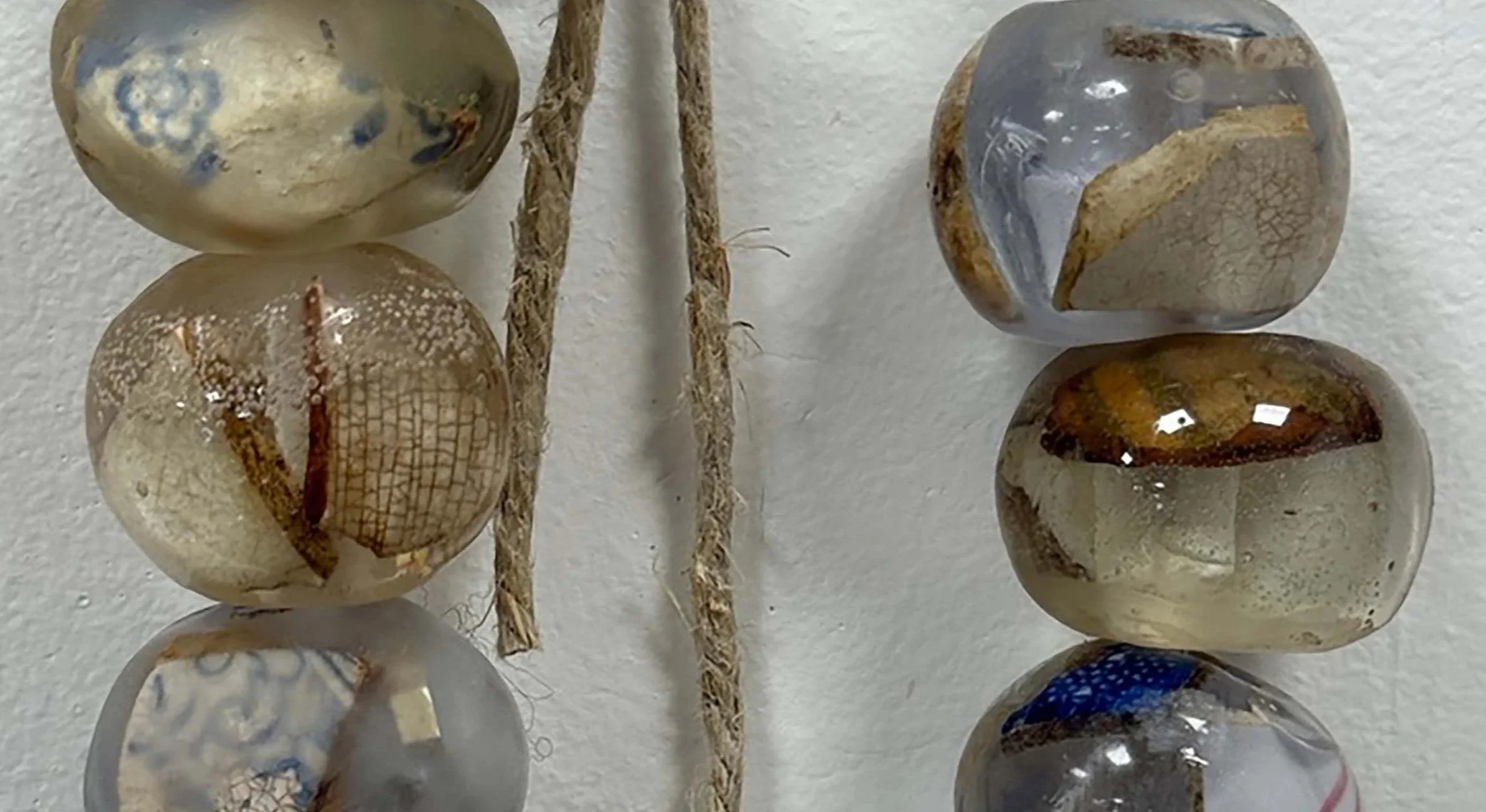 Close-up of six polished stones with different patterns and colors, arranged on a white surface, with two pieces of rope in the center.