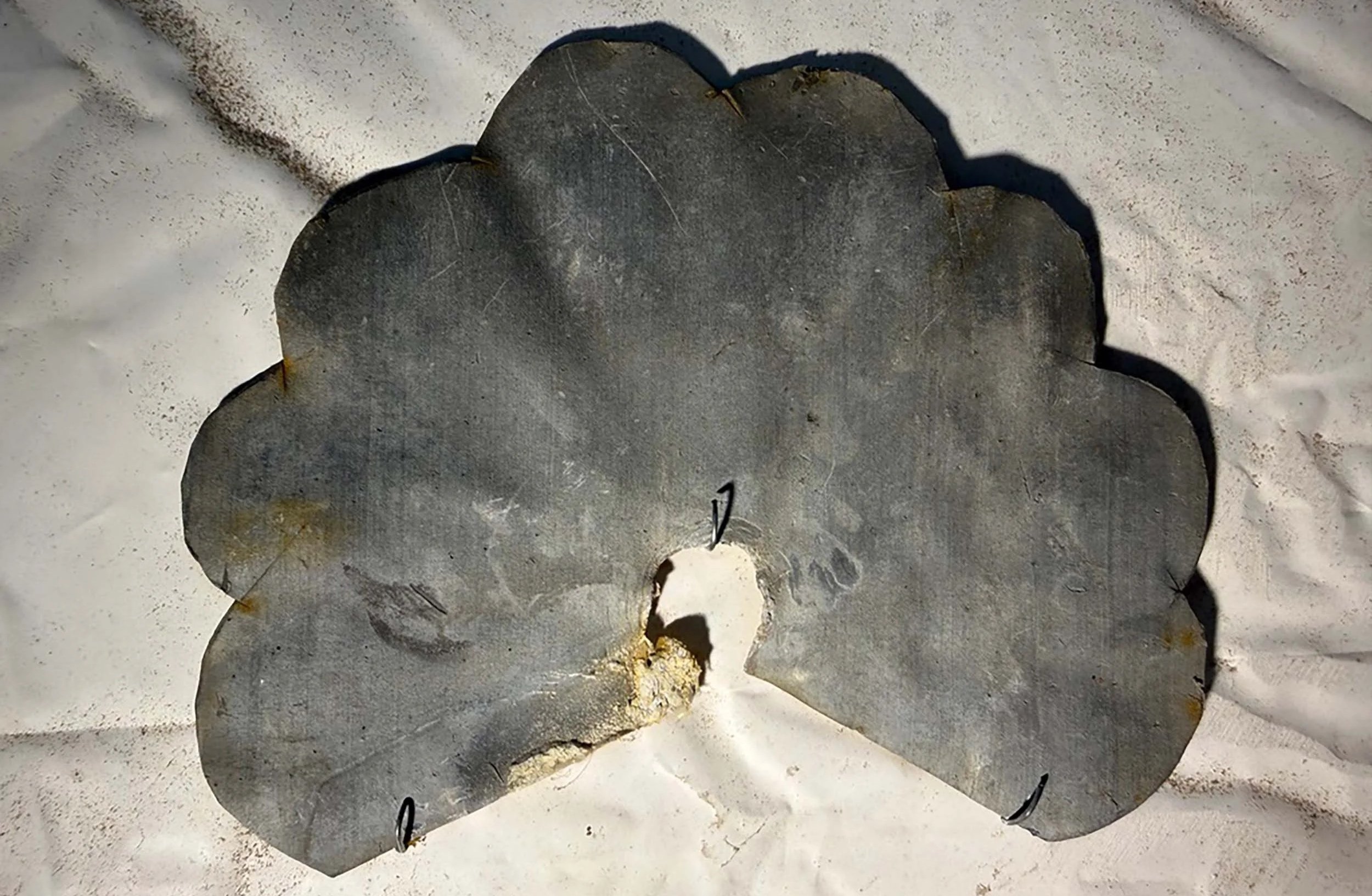 A close-up of a saw blade with some rust and corrosion, placed on a white surface.