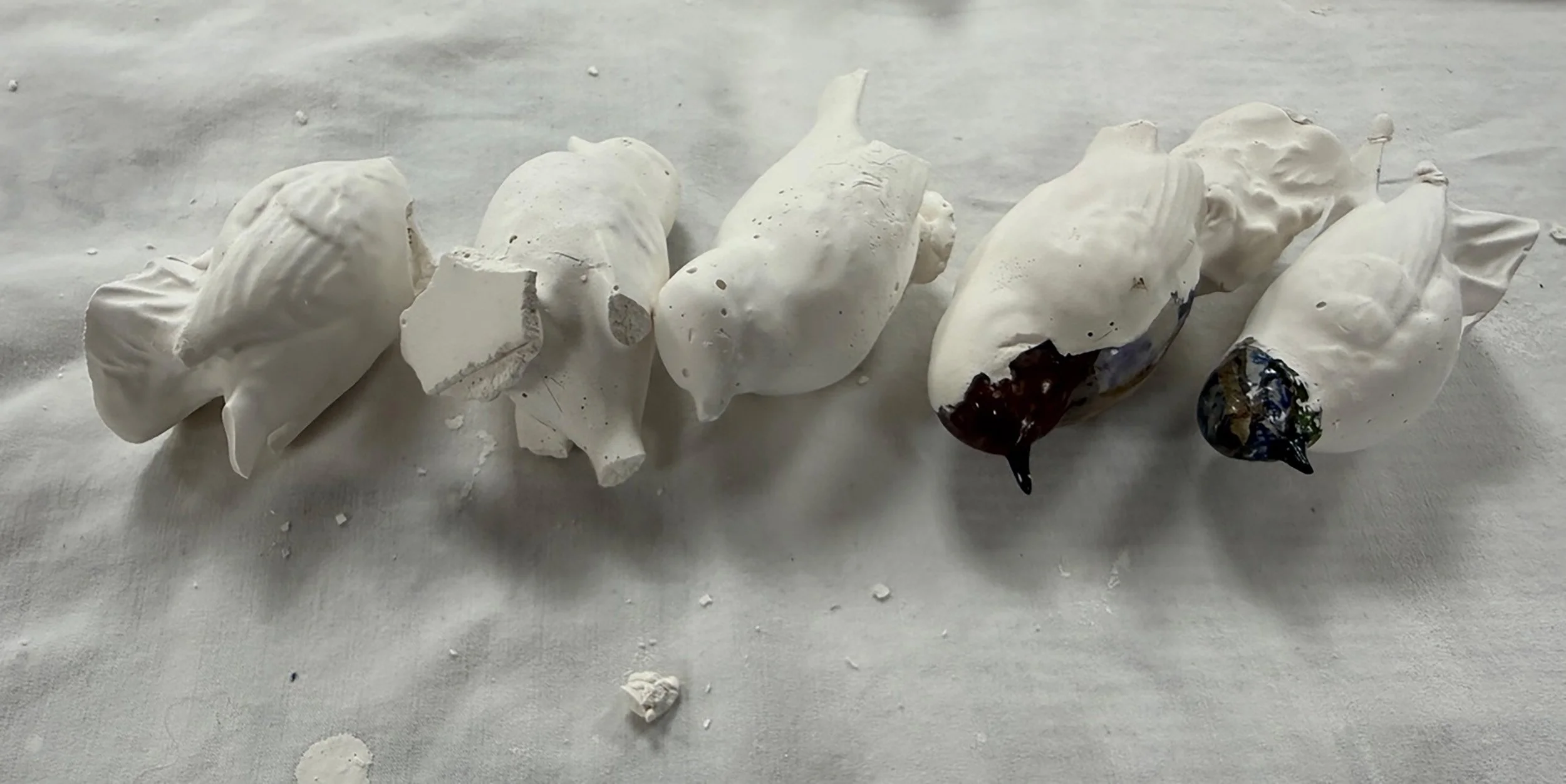 A row of six animal-shaped sculptures made of white material, with some having dark painted areas, lying on a light surface.