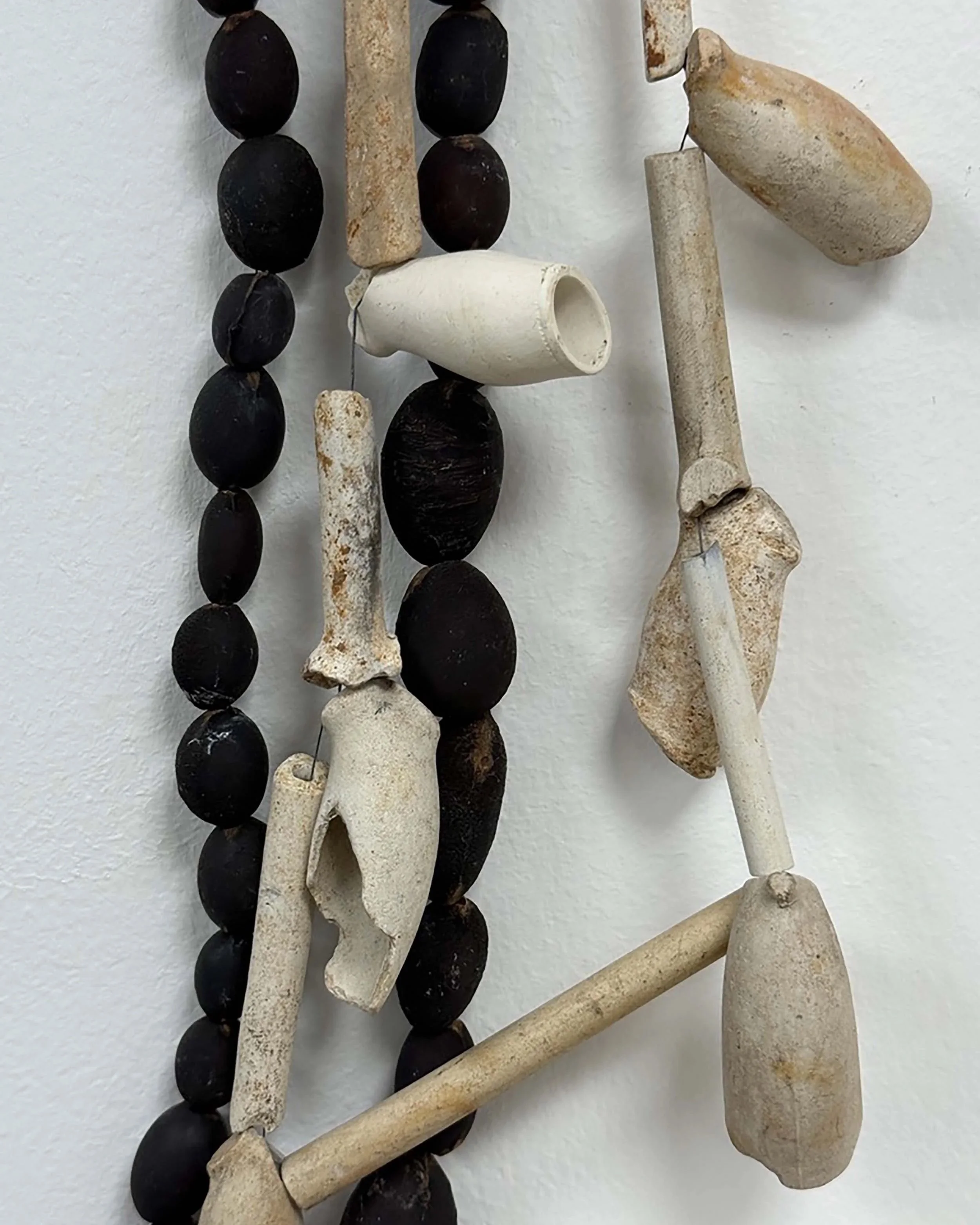 A close-up of a collection of objects including black beads, bone or ivory pieces, and small tools or parts arranged against a white background.