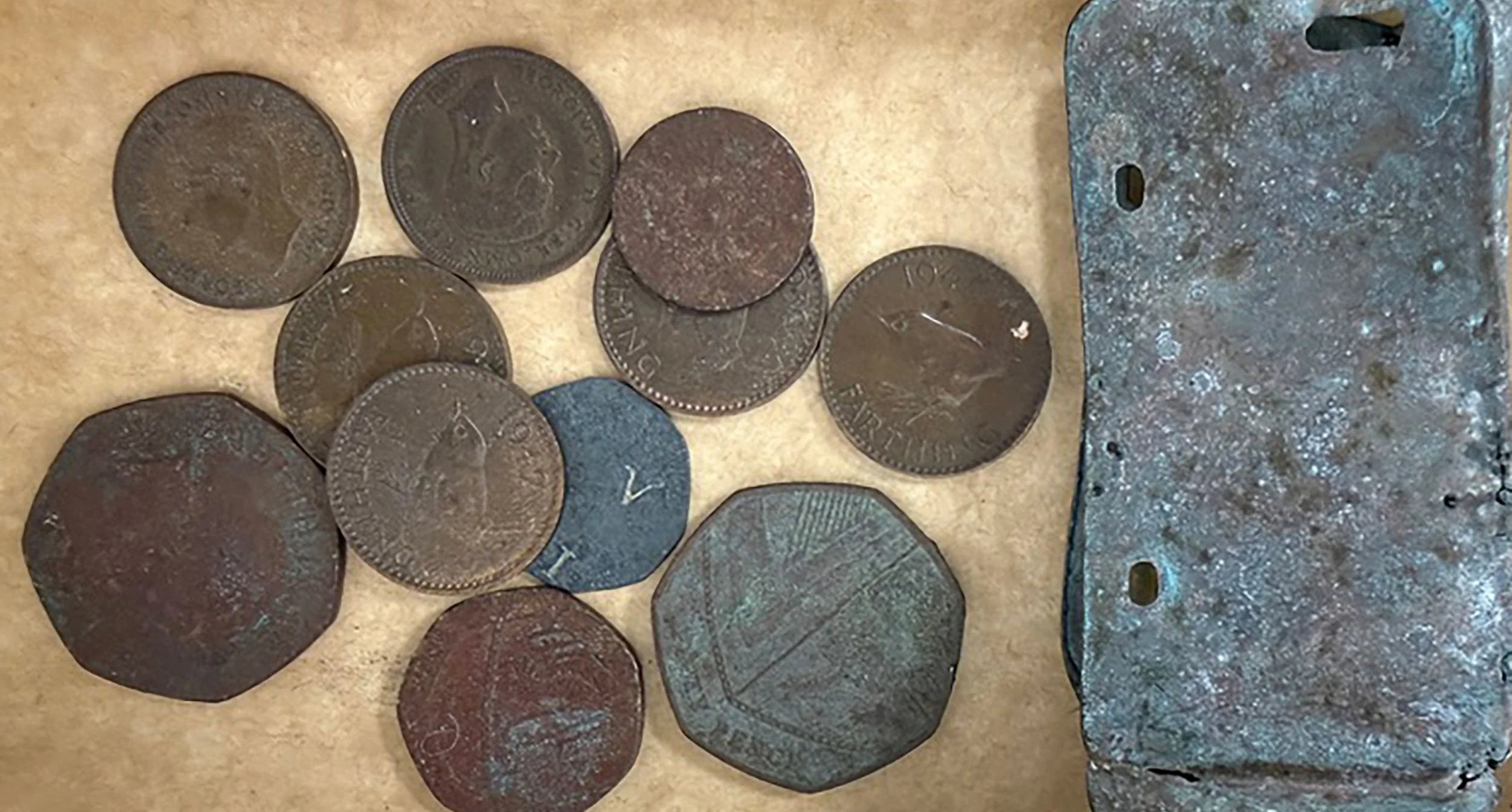 Collection of old, worn coins and a metal object with holes on a surface.