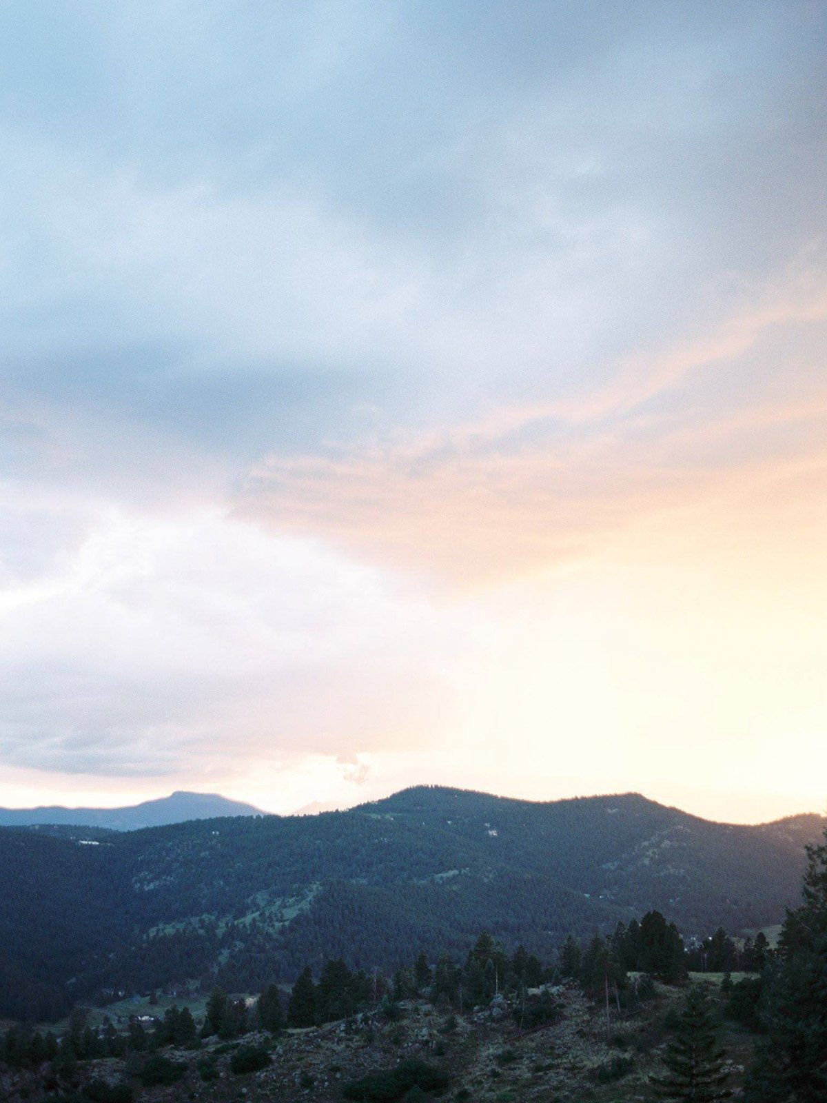 A landscape scene with mountains and a partly cloudy sky at dusk, showing soft pastel colors.