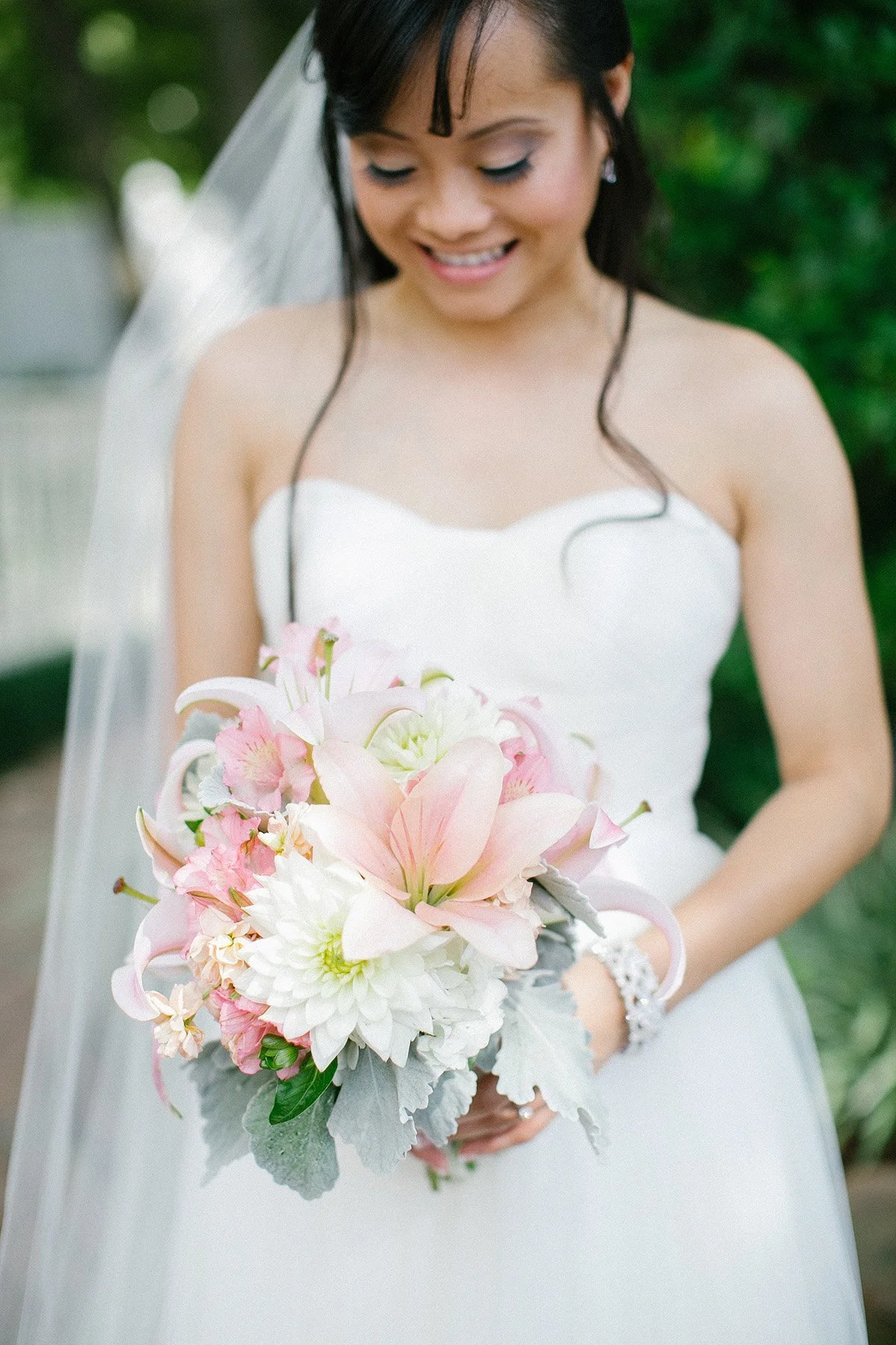 A bride in a white wedding gown holding a bouquet of pink and white flowers, smiling.