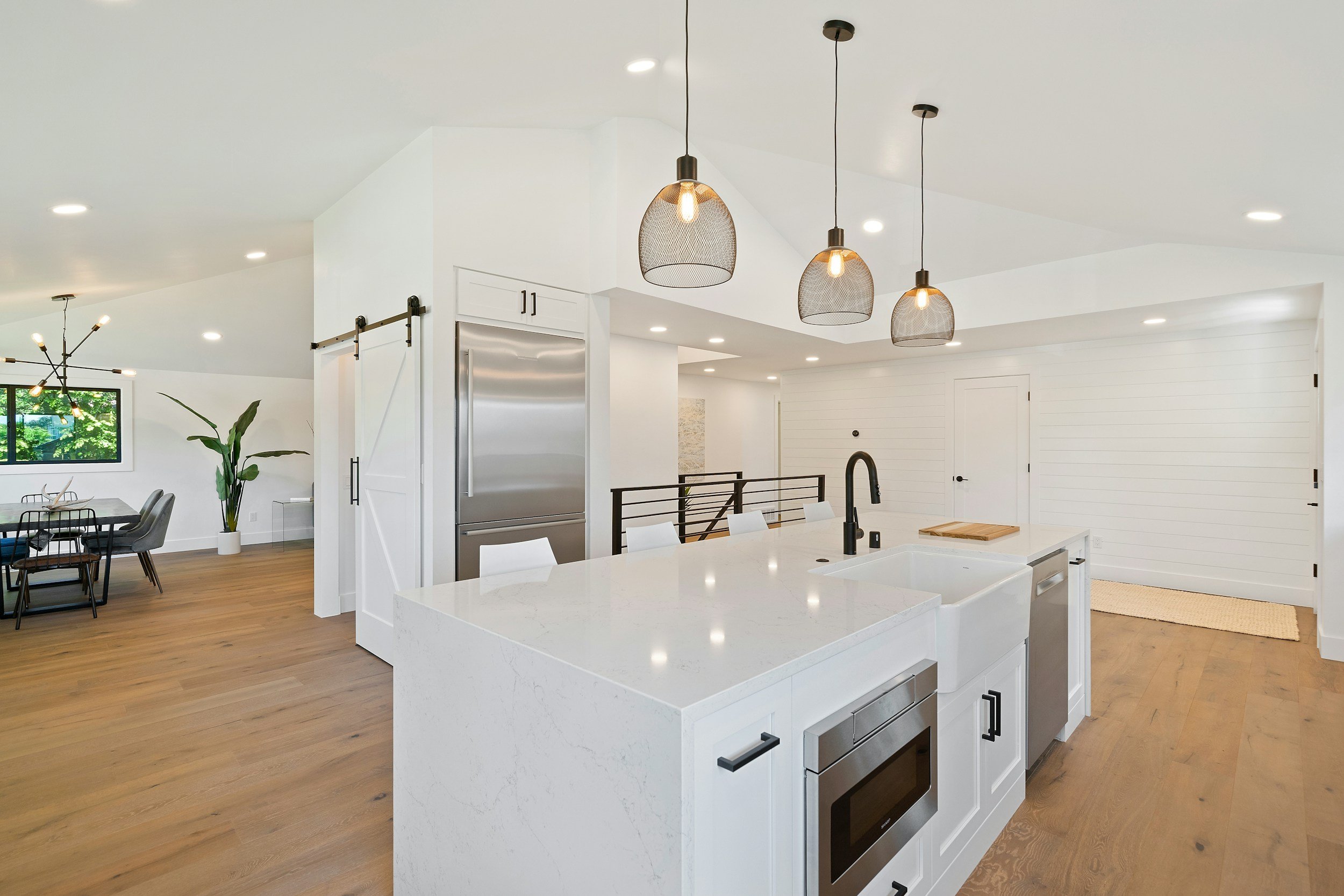 Modern kitchen with white cabinetry, marble island, black hardware, pendant lights, and hardwood floors.