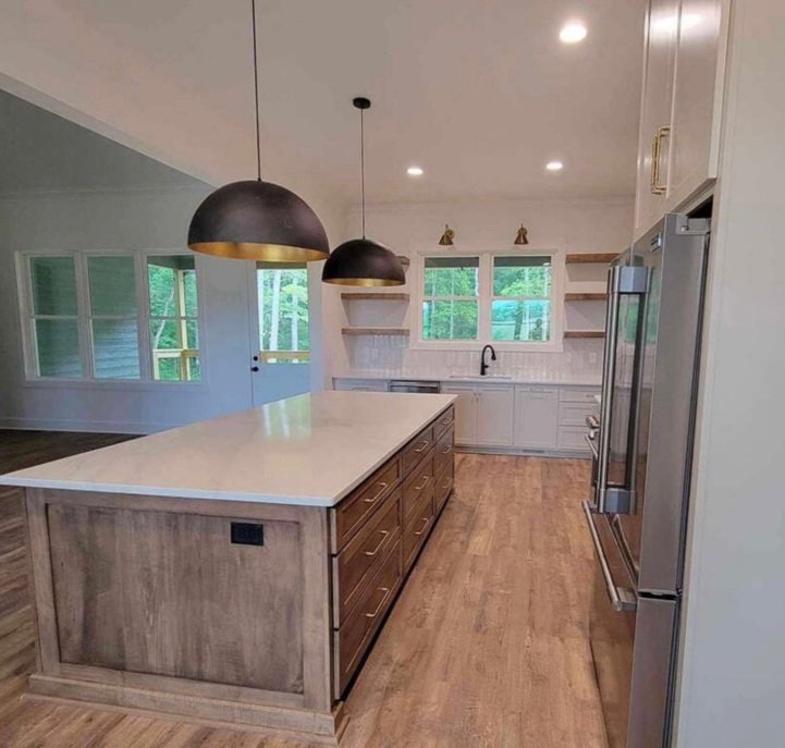 Modern kitchen with an island, white cabinets, a double oven, and large windows overlooking greenery.