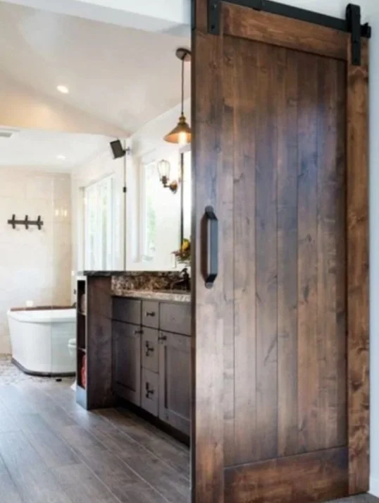 Interior view of a bathroom with a wooden sliding barn door, vanity with granite countertop, a bathtub, and a wall-mounted light fixture.
