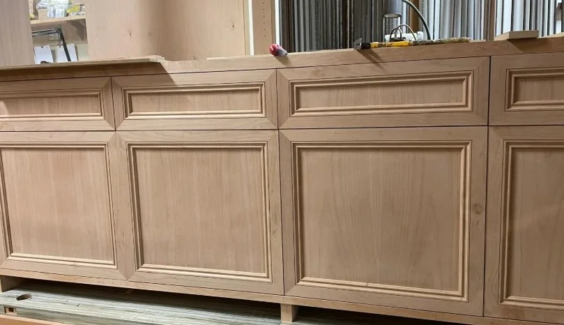 Painted wood cabinets inside a workshop or kitchen, with tools on the countertop and a window with curtains in the background.