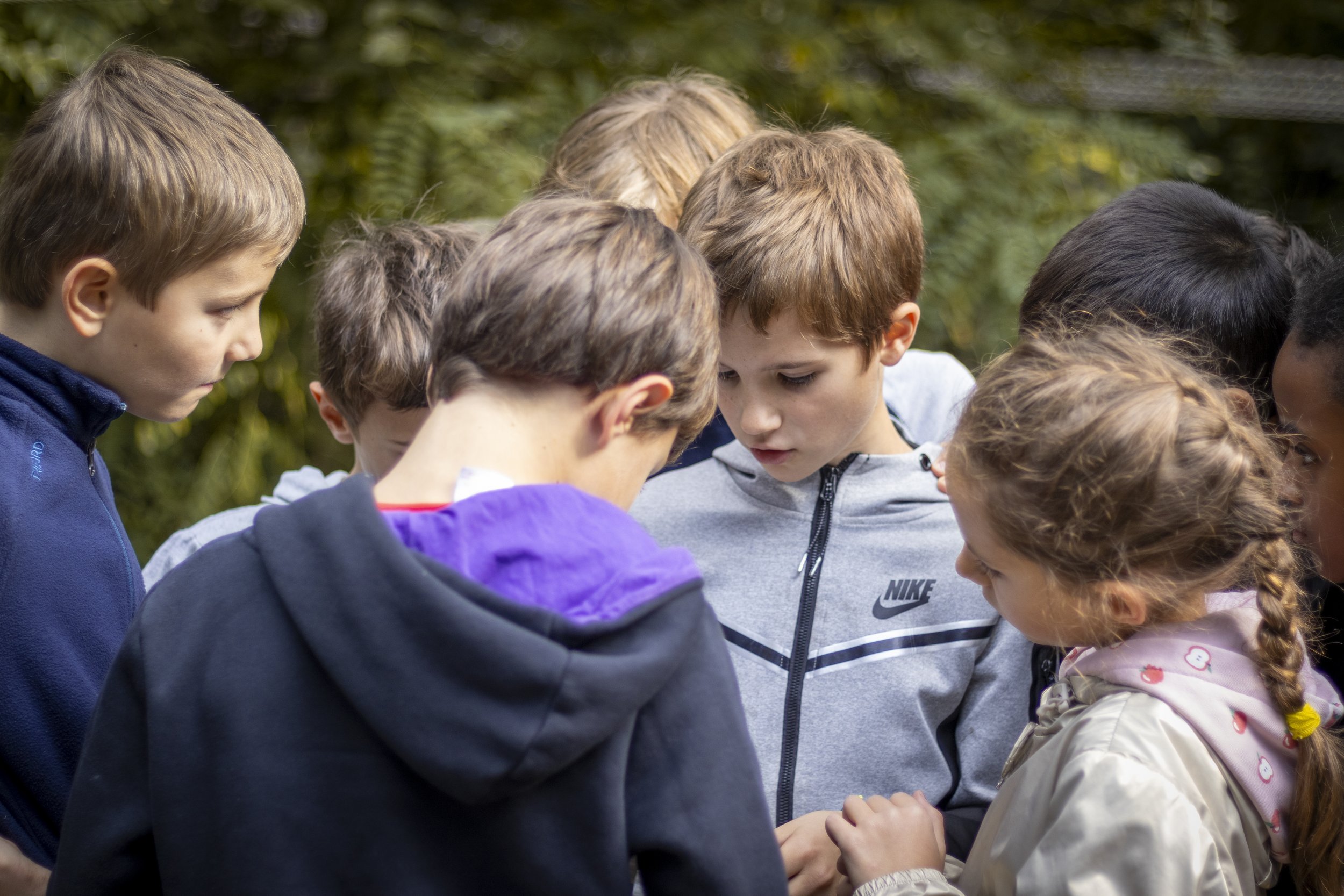 Groupe de jeunes enfants et adolescents réunis en cercle, concentrés sur une activité ou un échange dans un parc ou un jardin.