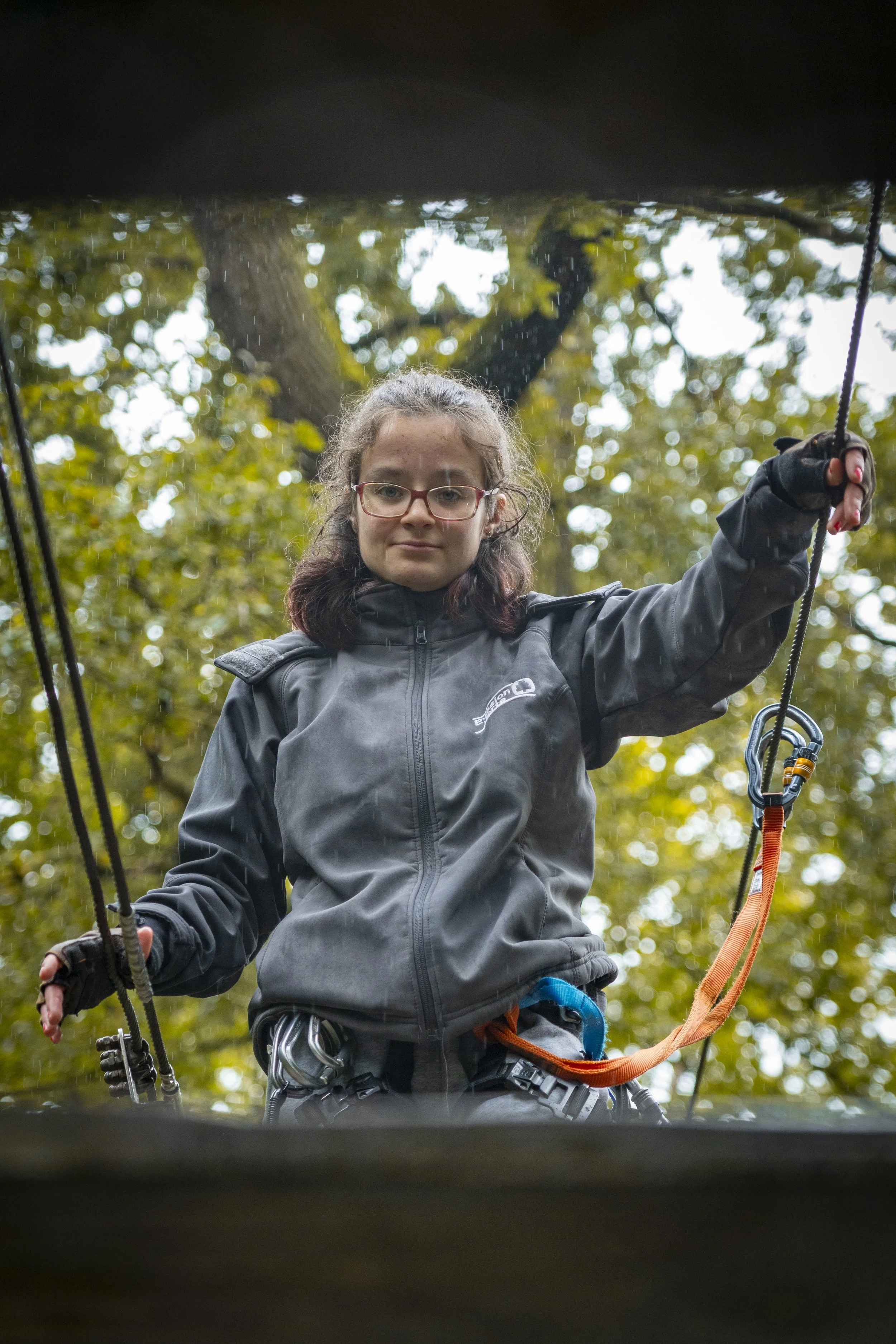 Jeune femme en vêtements d'escalade, tenant des cordes, dans un environnement forestier lors d'une activité d'escalade ou d'alpinisme.