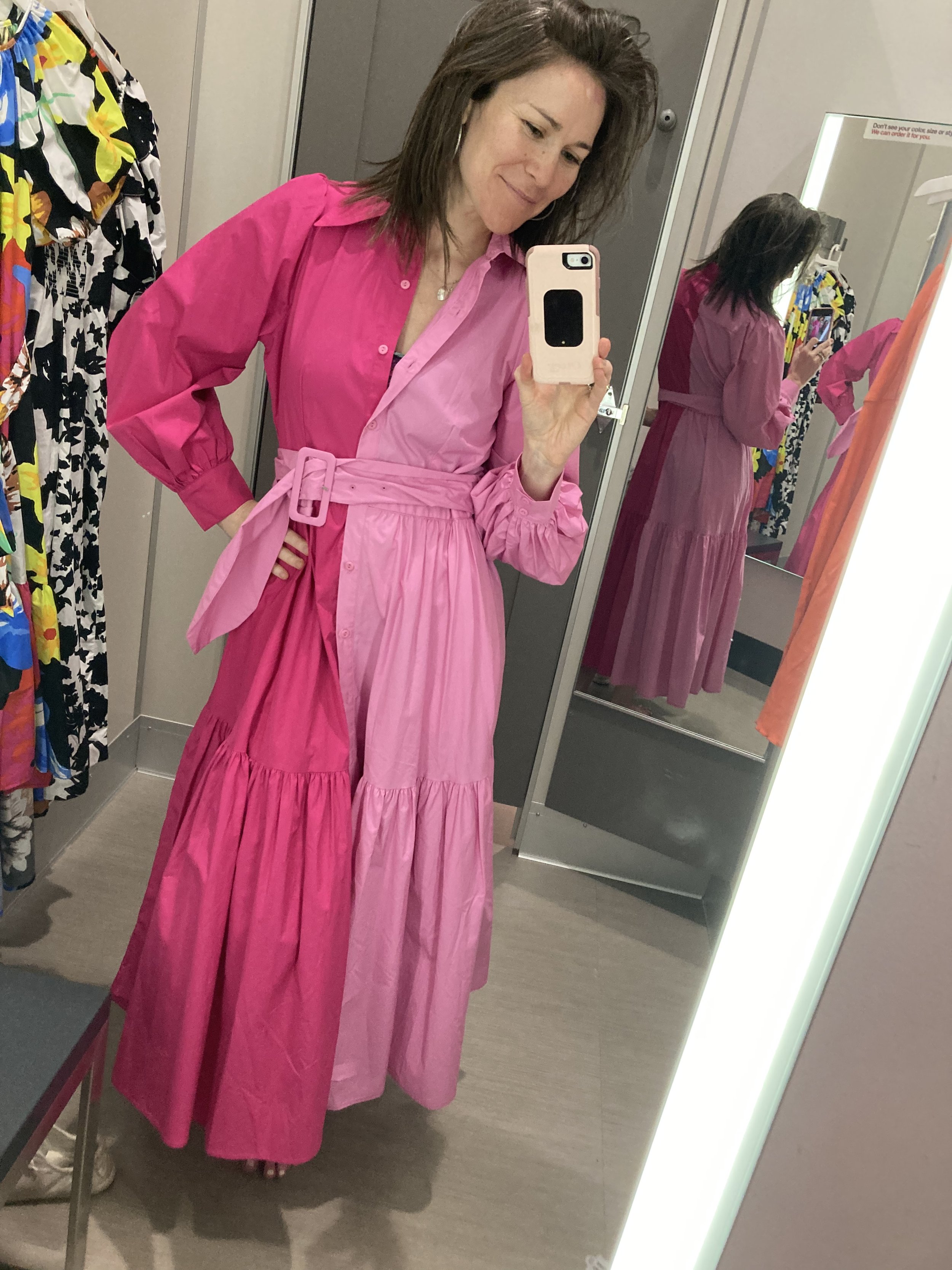 Woman trying on a pink dress in a fitting room, taking a selfie in front of a mirror.