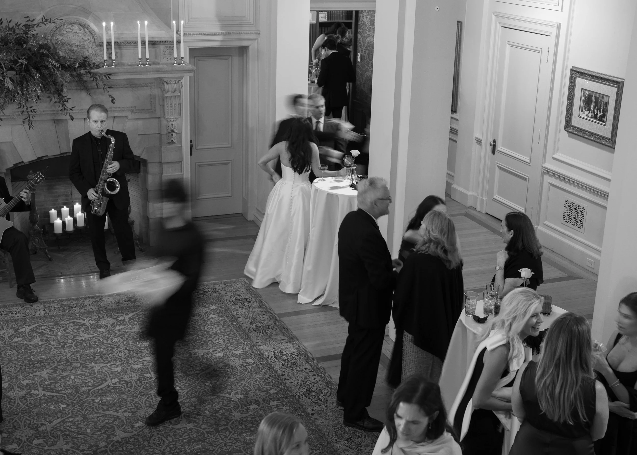Guests dancing at a wedding reception, with a live band performing near a fireplace and framed artwork on the walls.