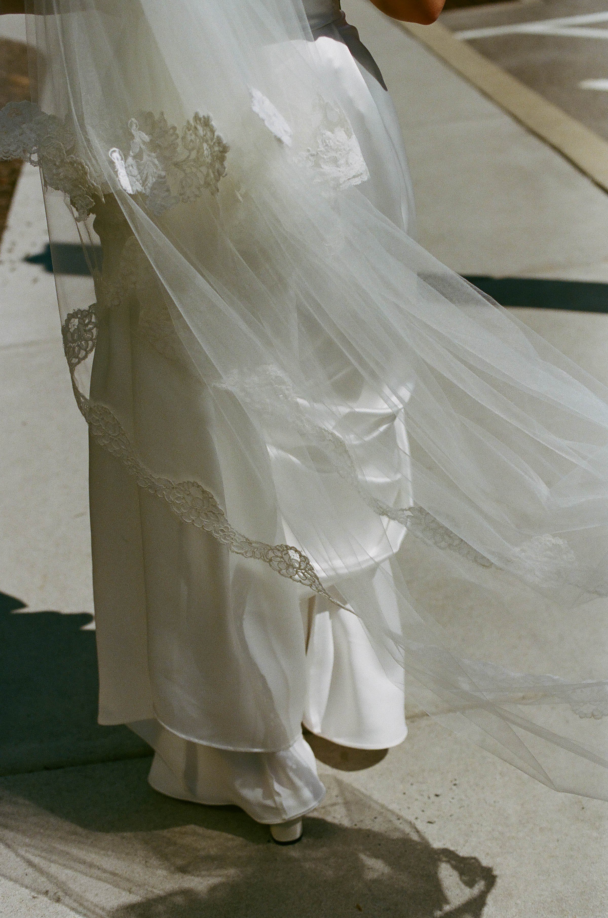 A wedding dress with lace detailing and a long flowing train, displayed on a mannequin.