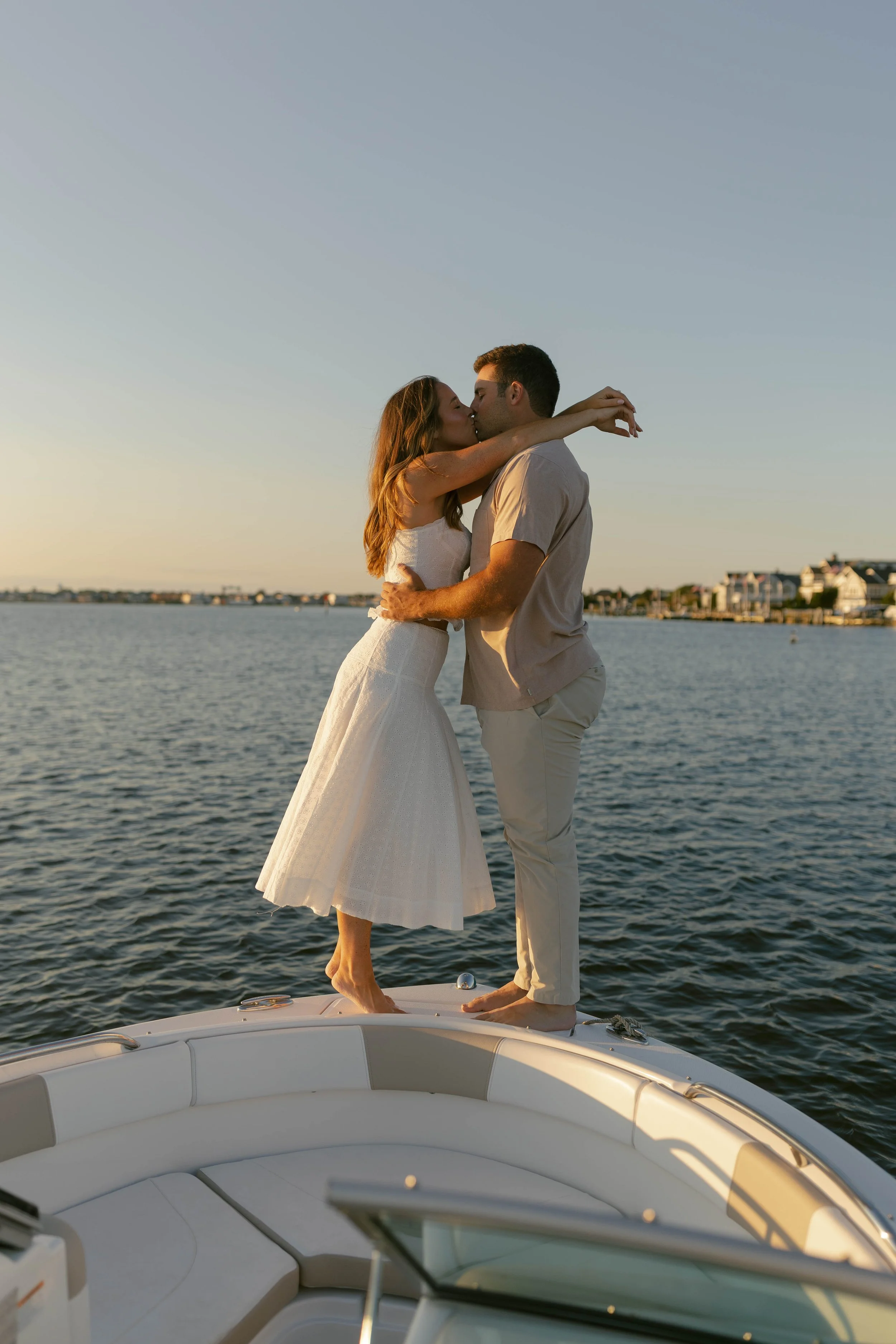 A couple is kissing on a boat at sunset with water and houses in the background.