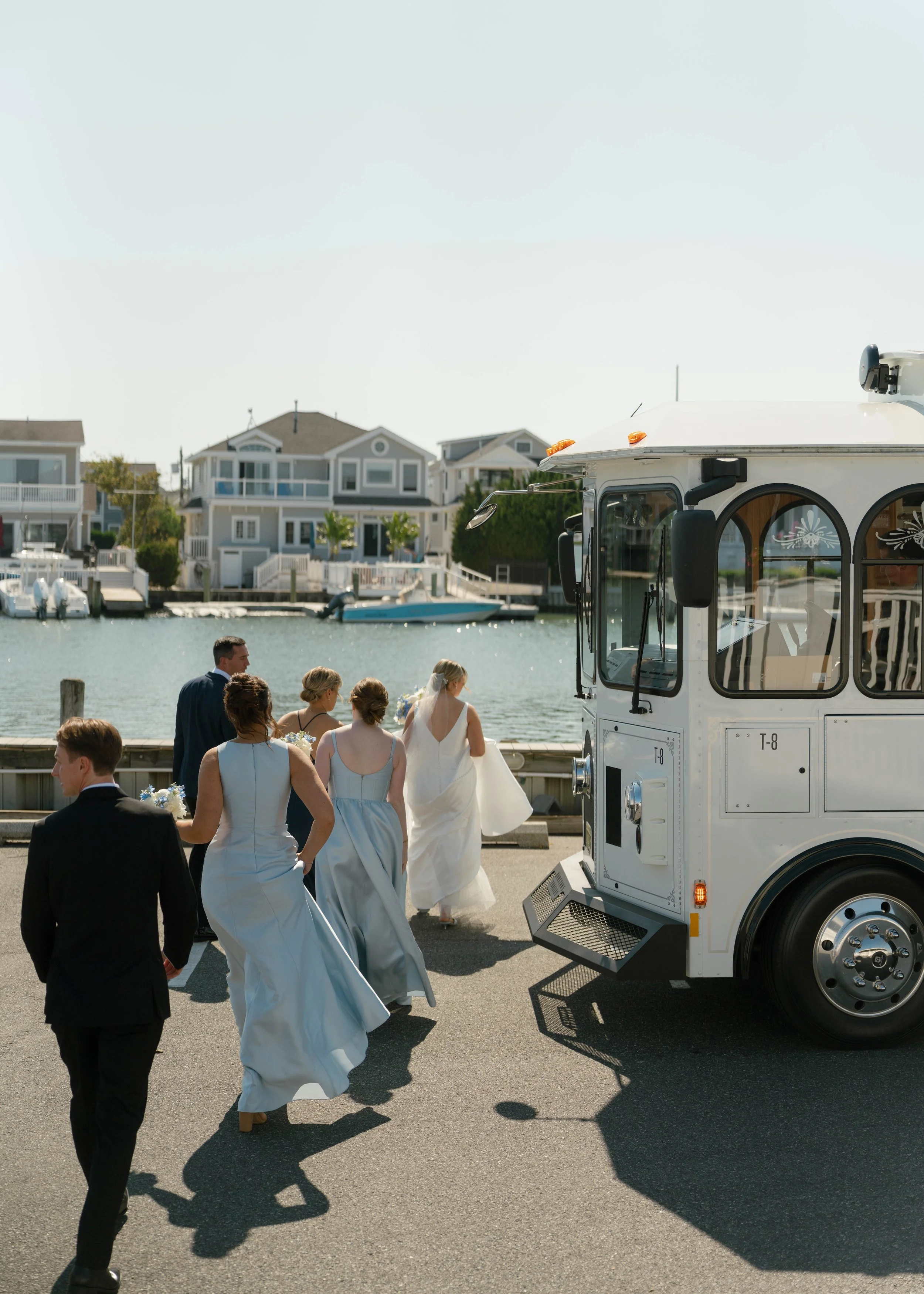 A wedding party arriving at a waterfront on a sunny day, with a white ice cream truck parked nearby.