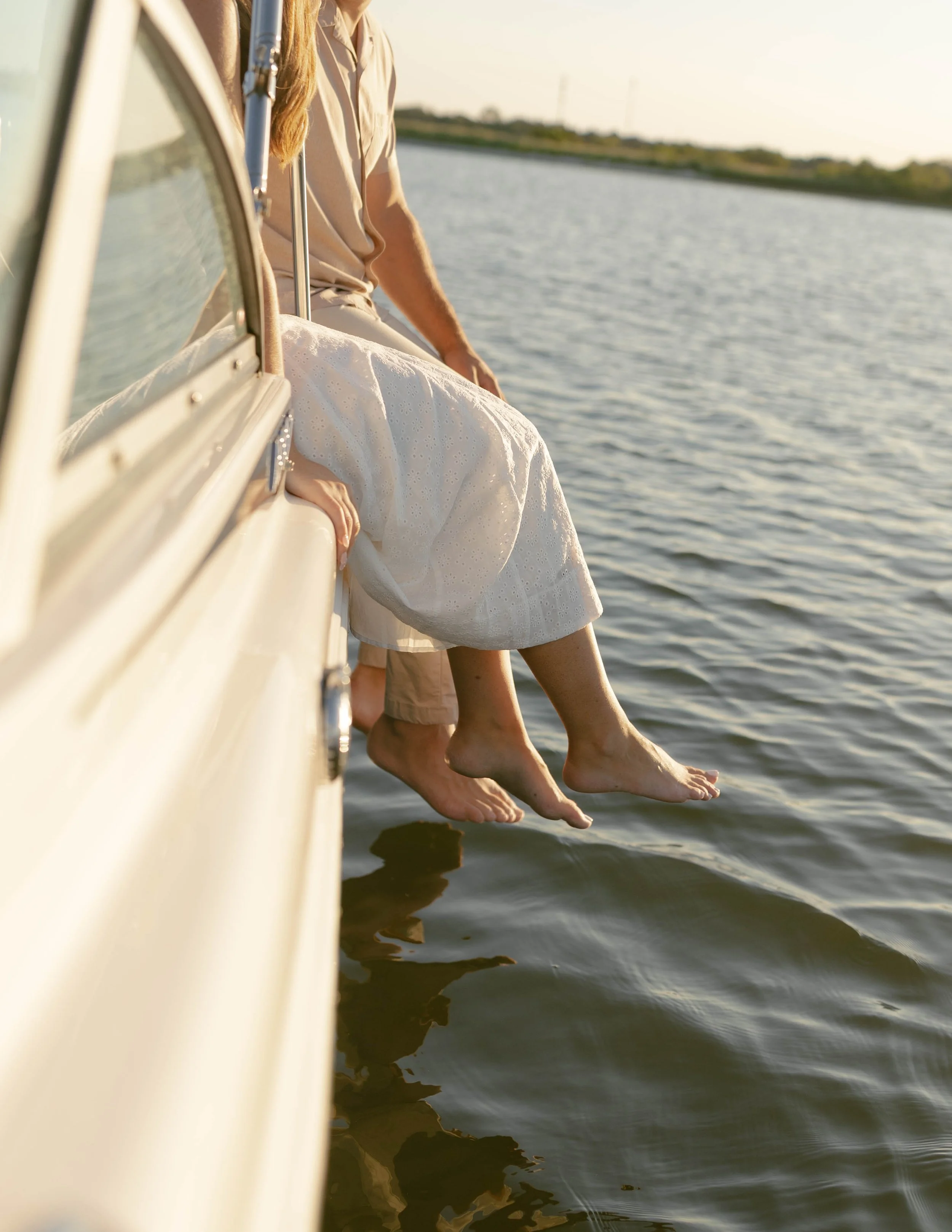 Two people sitting on the edge of a boat with their legs hanging over the water during sunset.