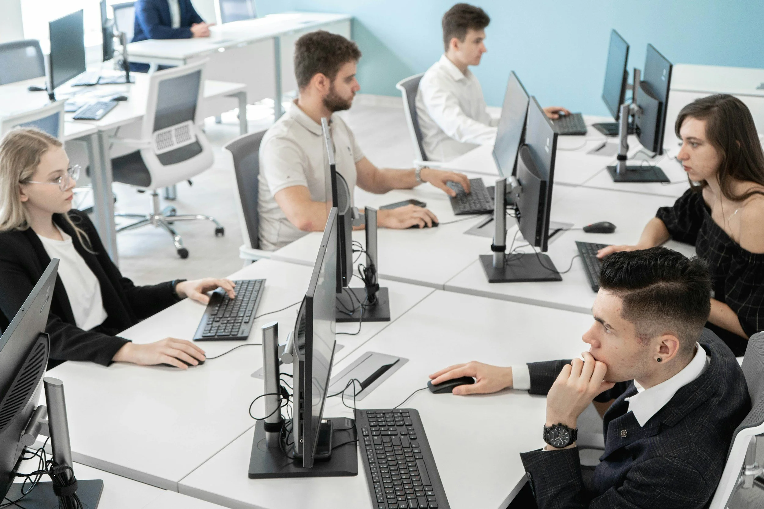 A bright room with blue walls and several men seated at their pc workstations.