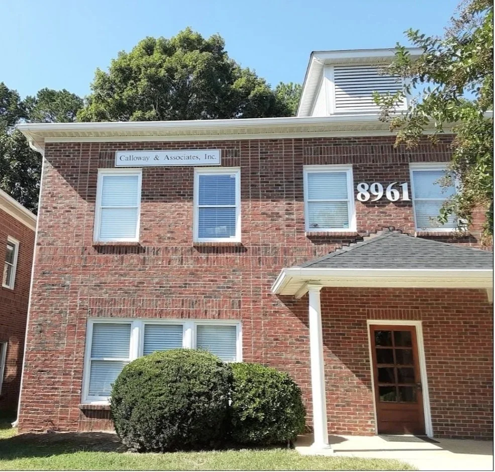Brick commercial building exterior with address number 8961 and trees under a blue sky.