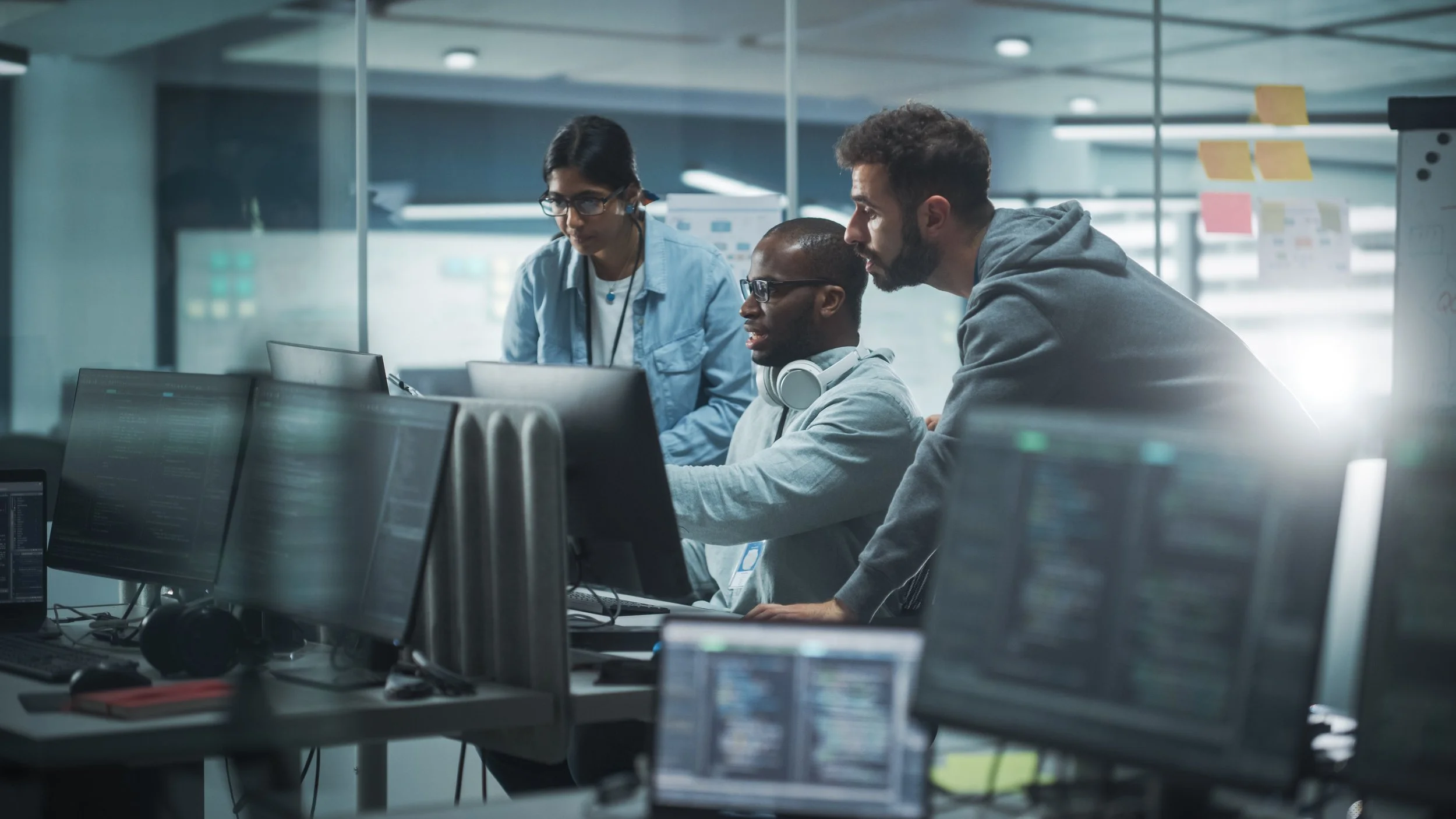Three men in a computer lab looking at a computer screen together.