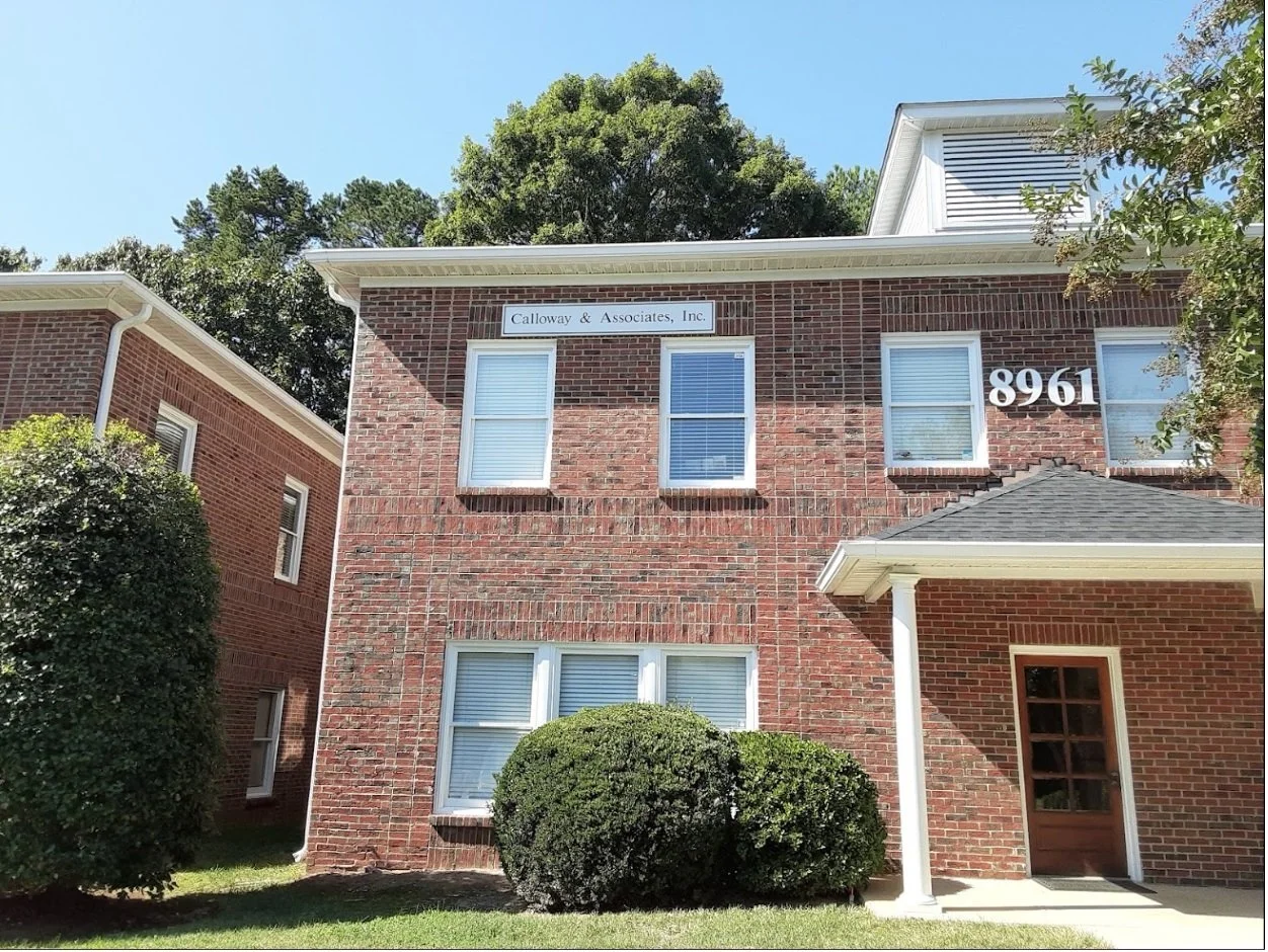 Brick commercial building exterior with address number 8961 and trees under a blue sky