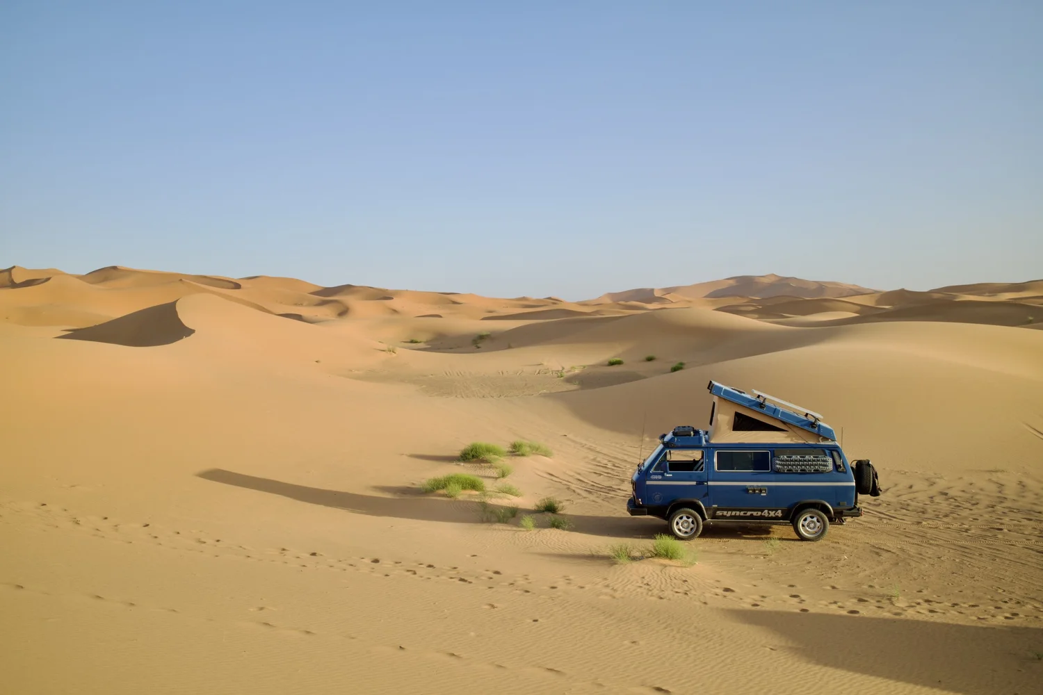 Blue Volkswagen Syncro camper travelling among desert dunes