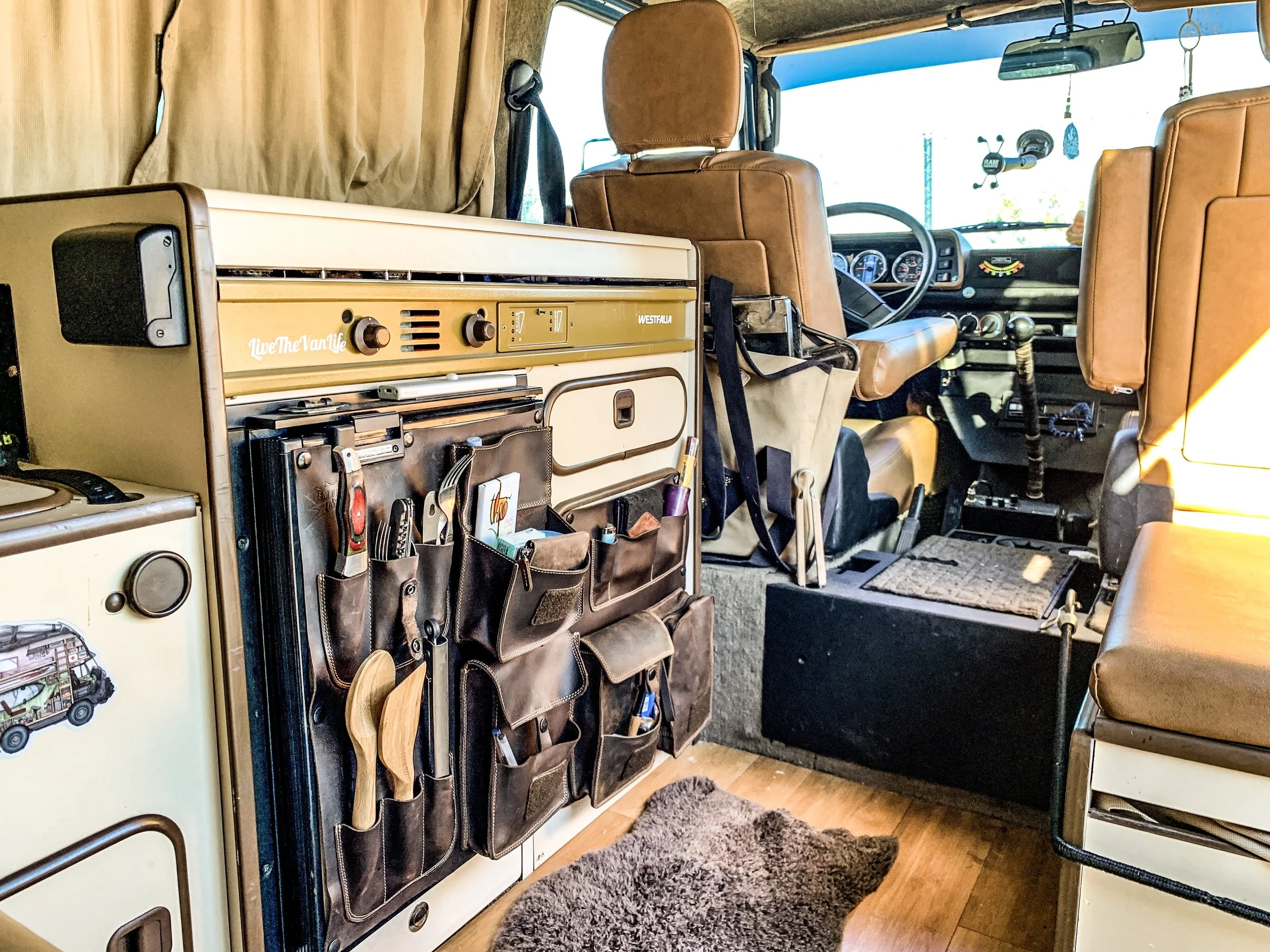 The interior of a vintage van with brown leather seats, a wall organizer with tools and other items, and a view of the driver's seat and dashboard.